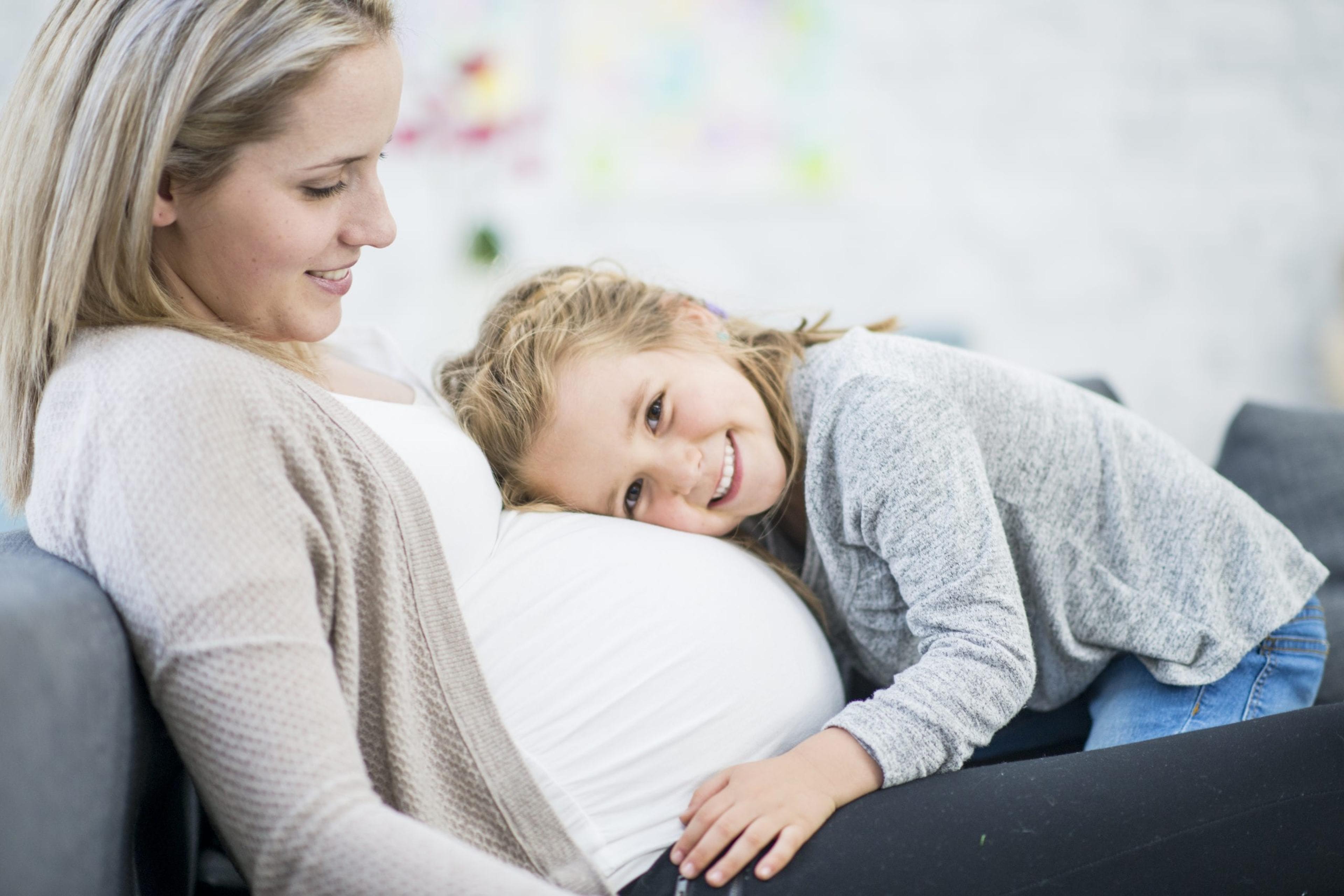 A pregnant woman and her young daughter laying on her stomach