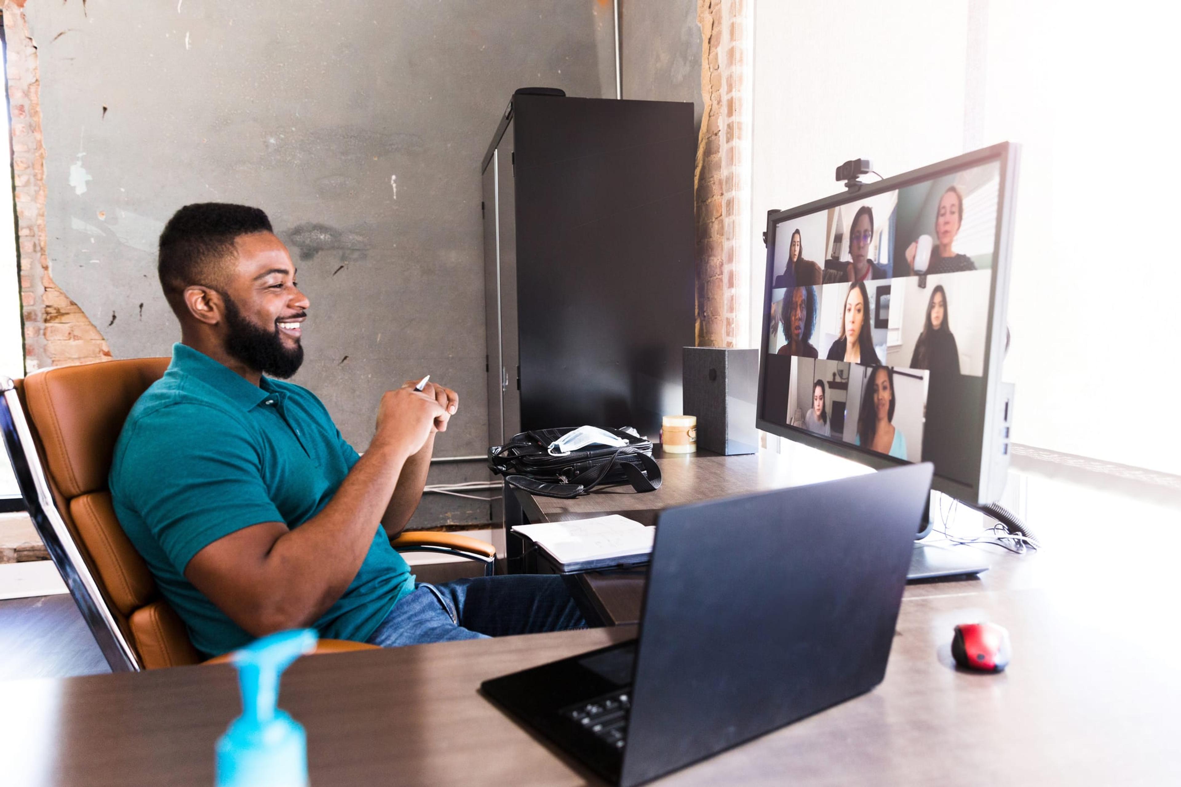 Black man sits at computer talking to several individuals in a virtual video call.