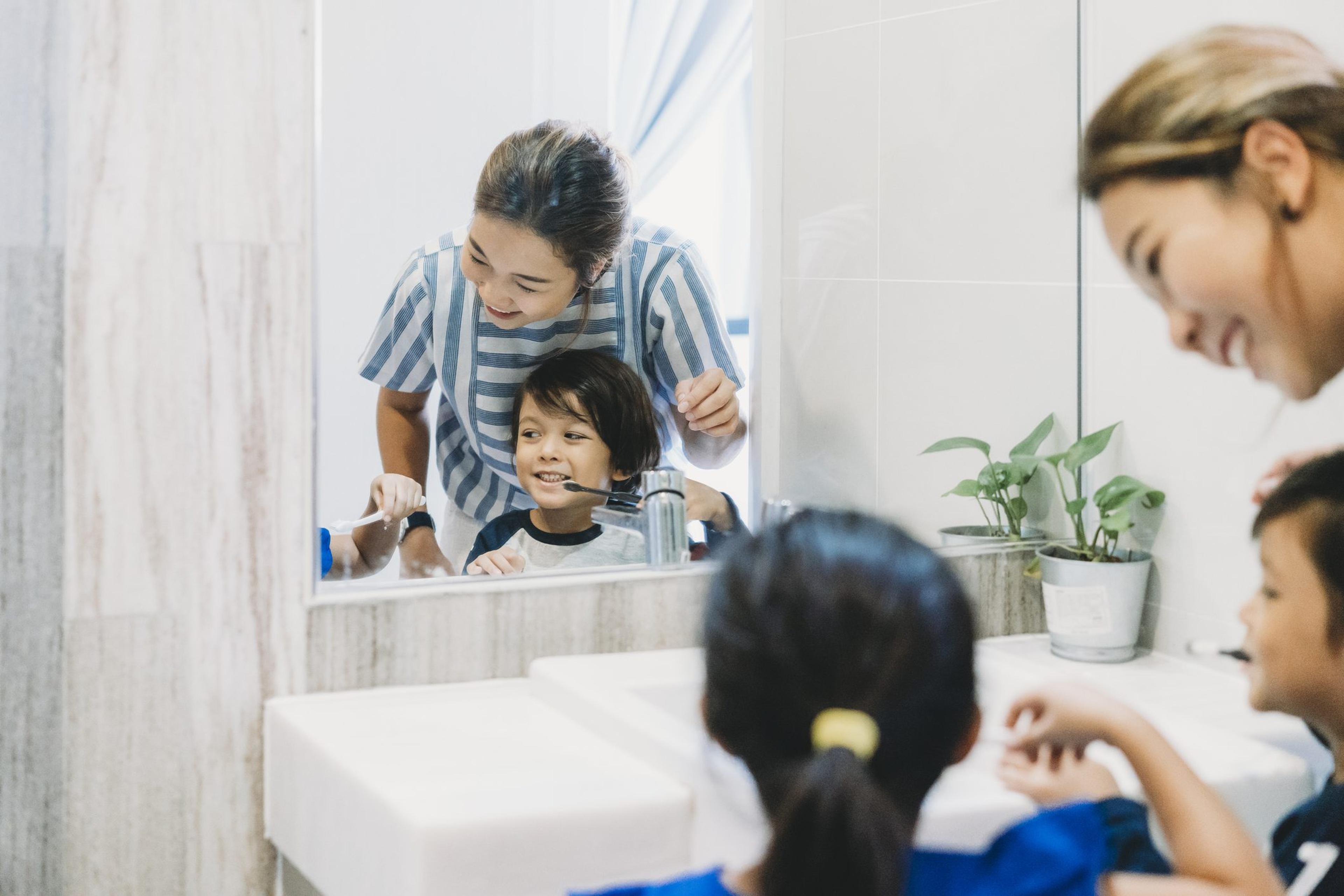 Brother and sister brushing their teeth with mom to keep up their oral health in the winter