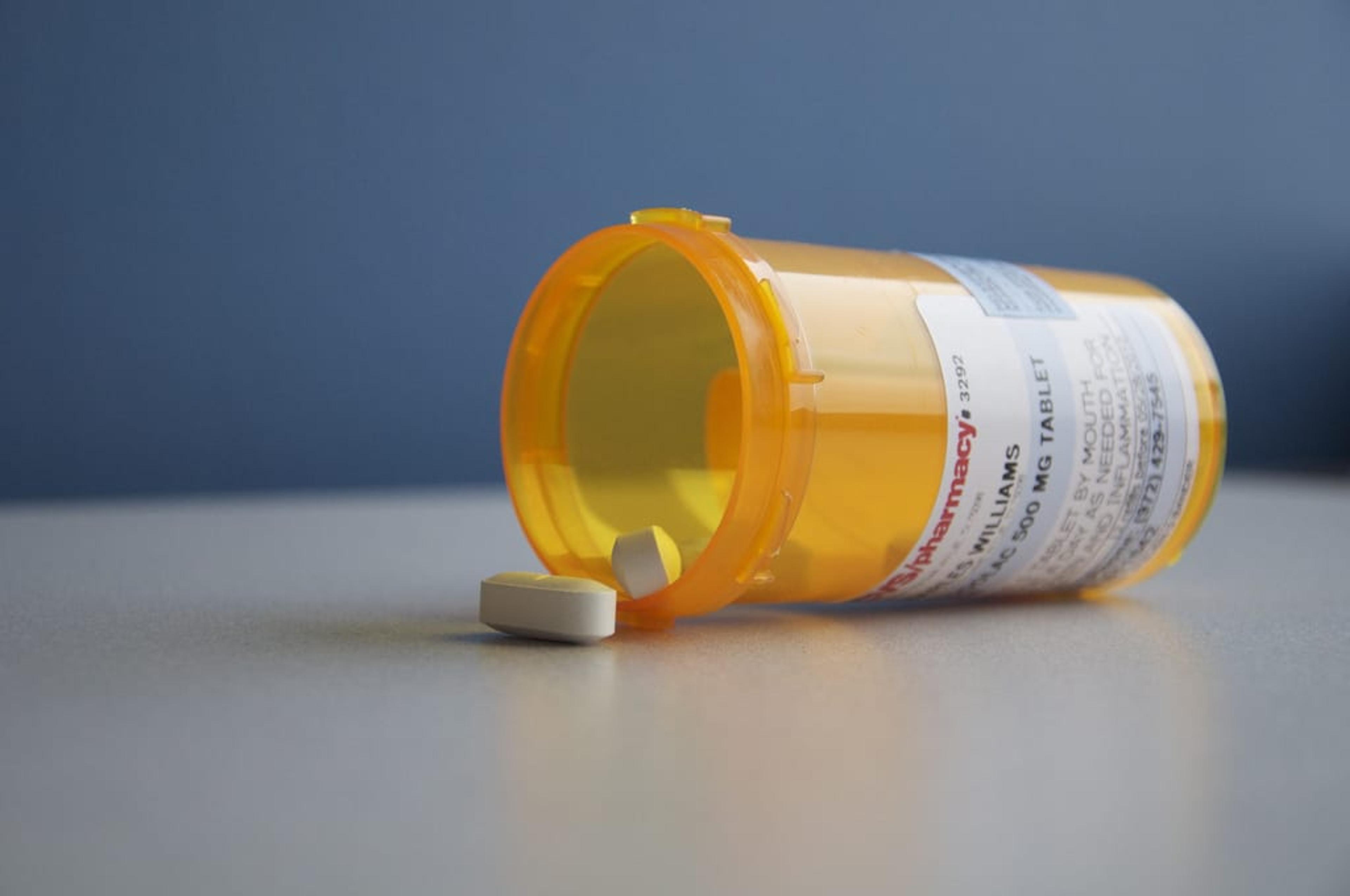 Image of a prescription medication bottled tipped on its side with pills spilling out on table.