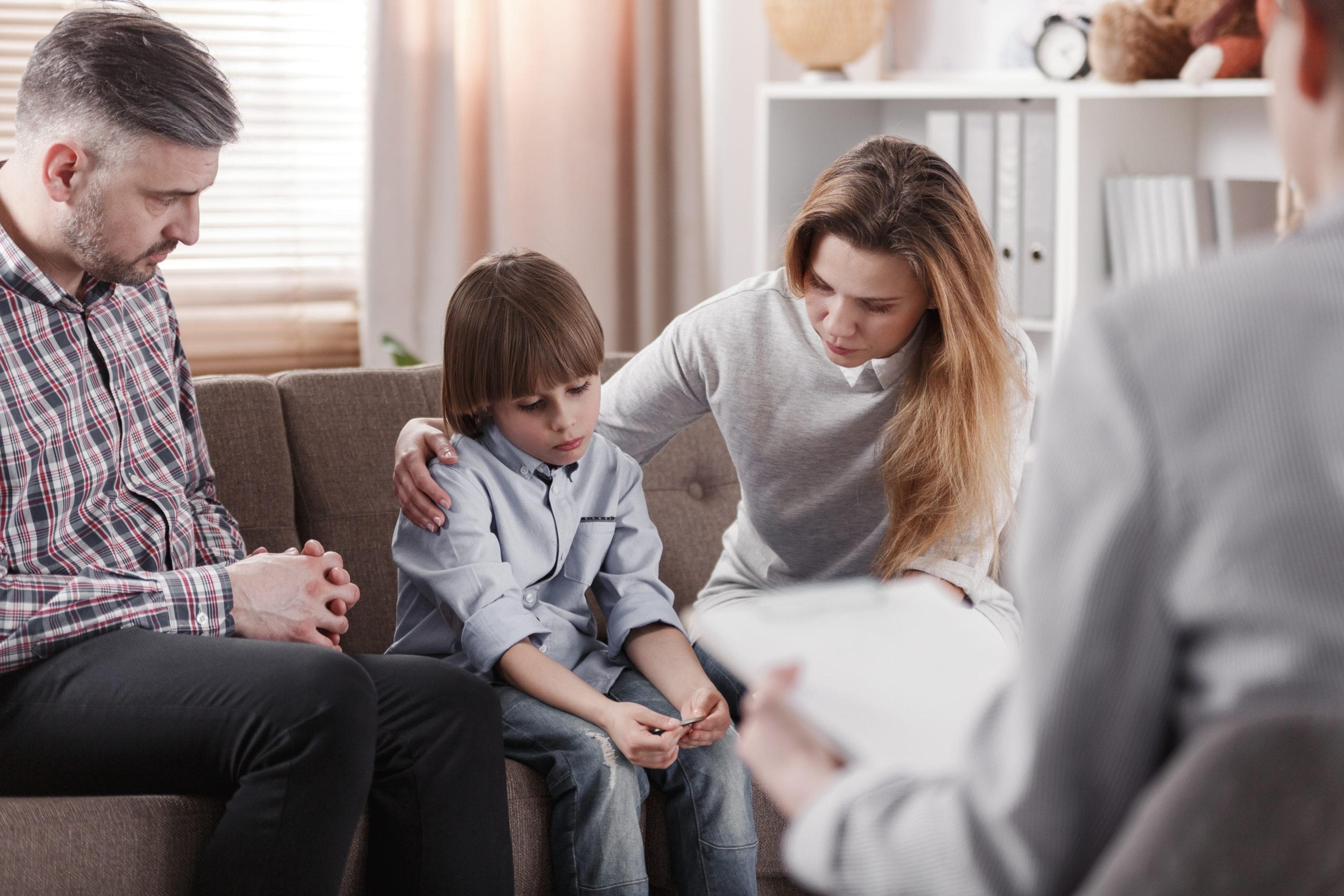 Mother hugging her autistic son, sitting next to a father during a family therapy