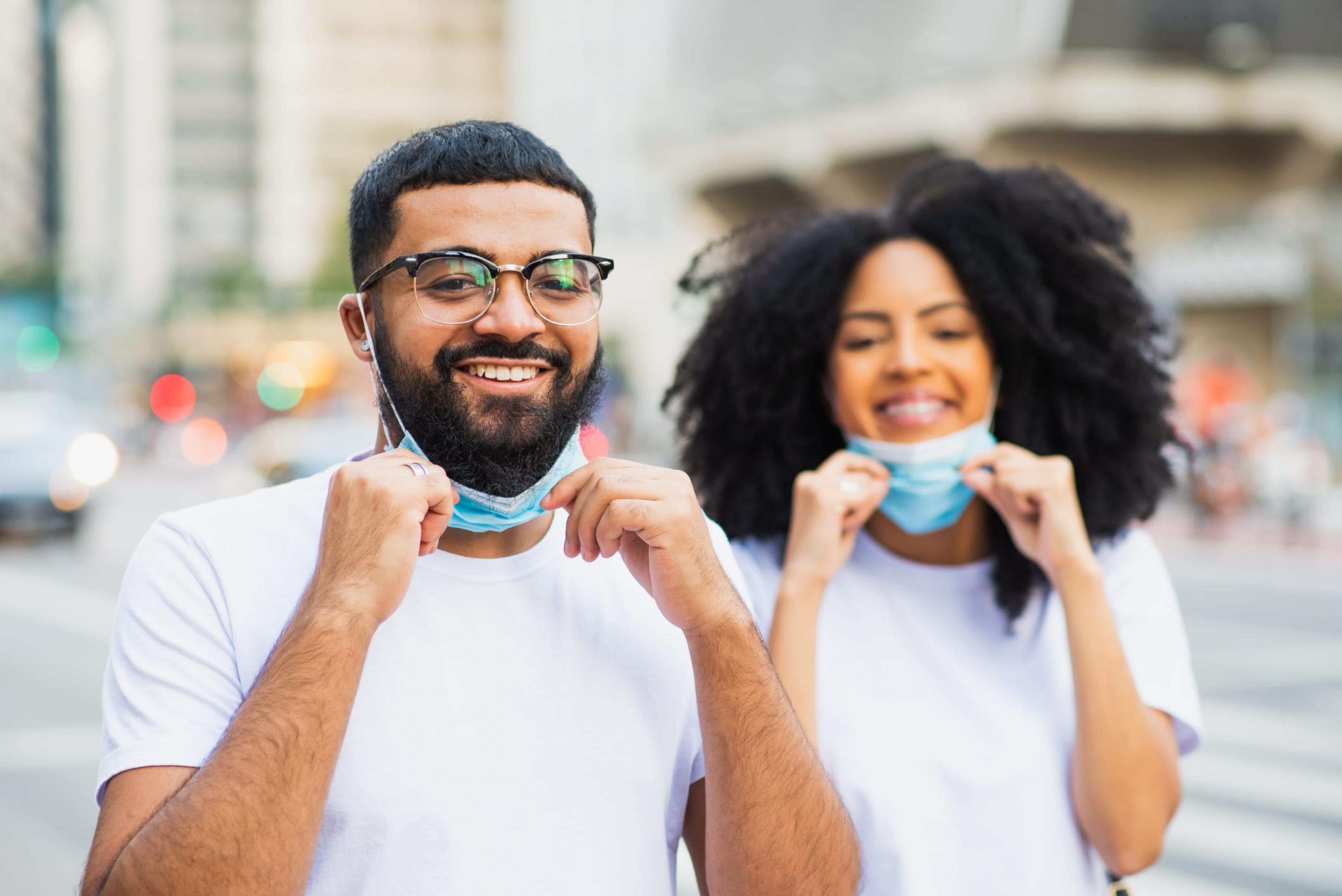 Two young people smiling and pulling down their masks outside