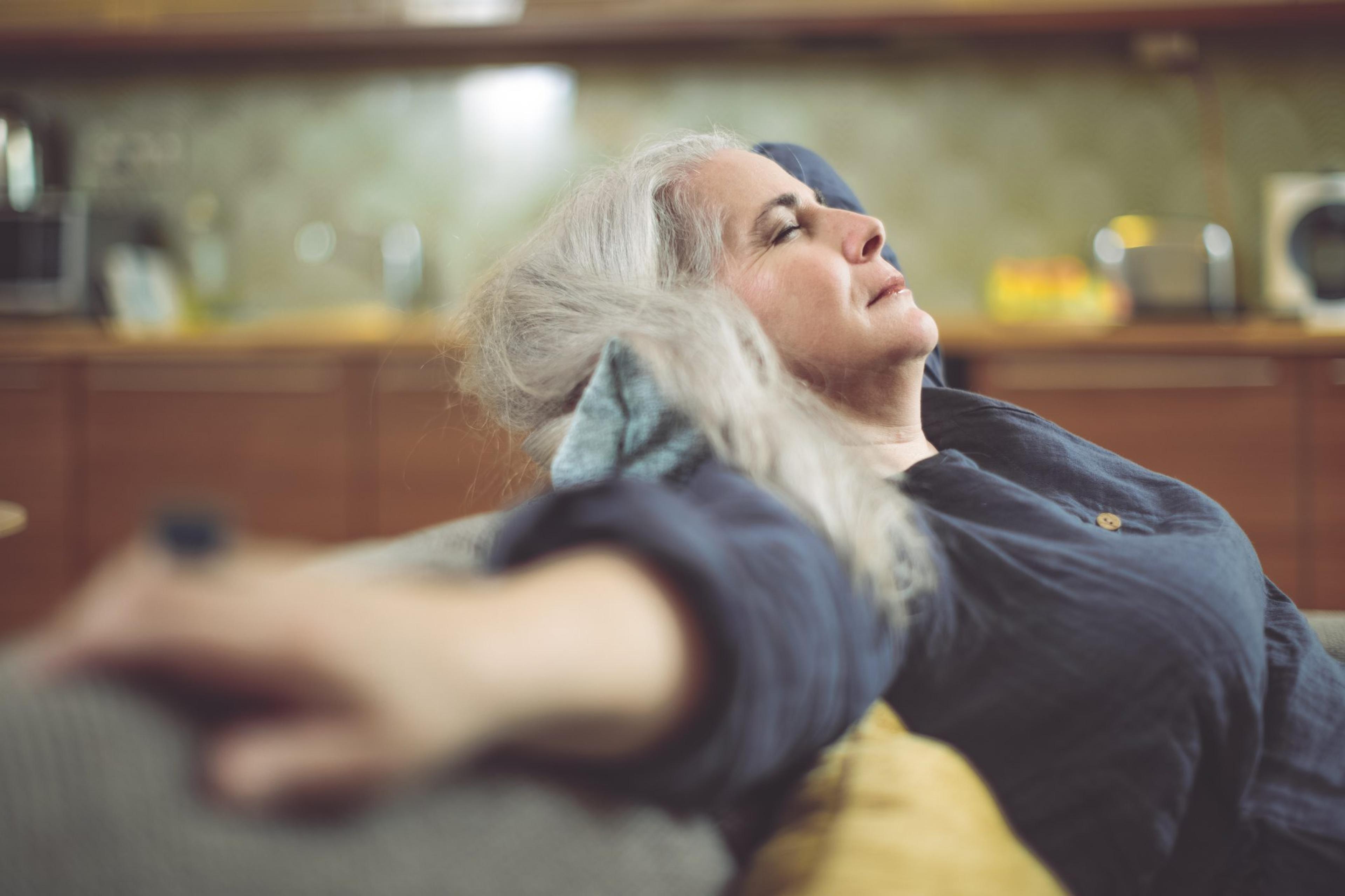 Woman recovering from cataract surgery leans back on her couch at home with her eyes closed