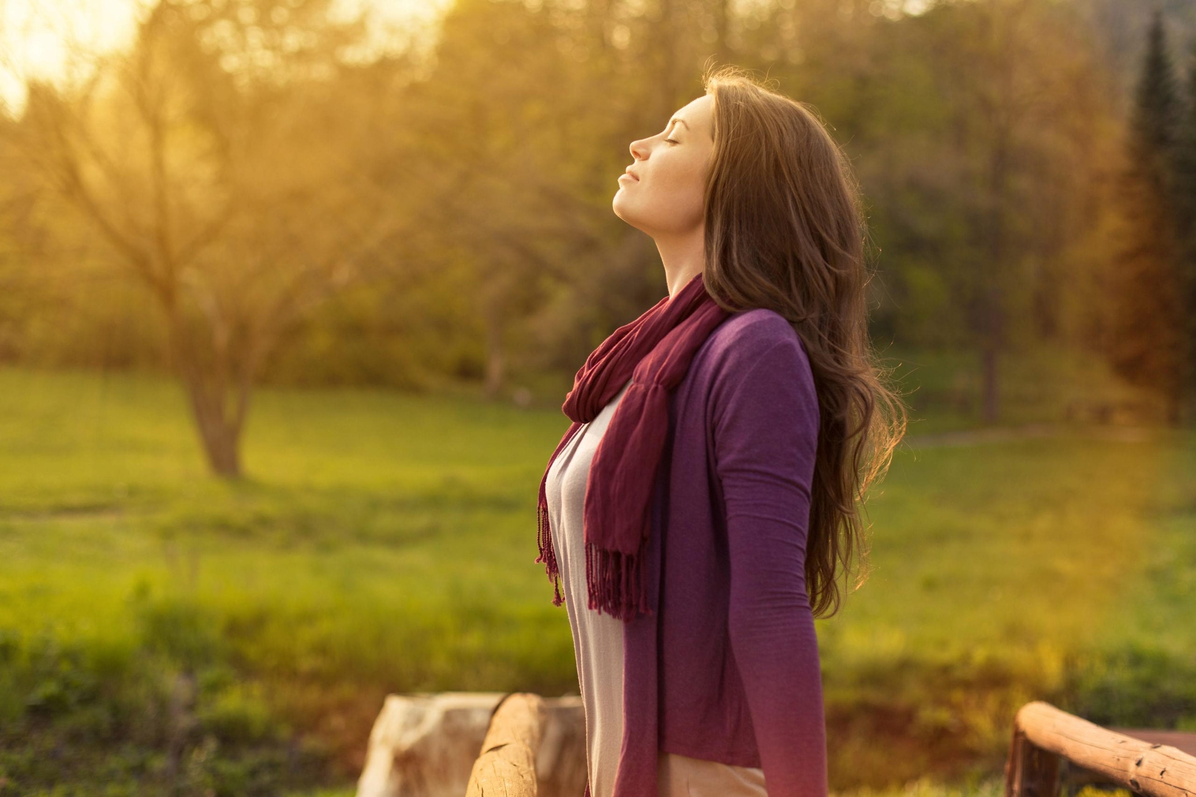 Woman with arms outstretched facing the sun, enjoying fresh air