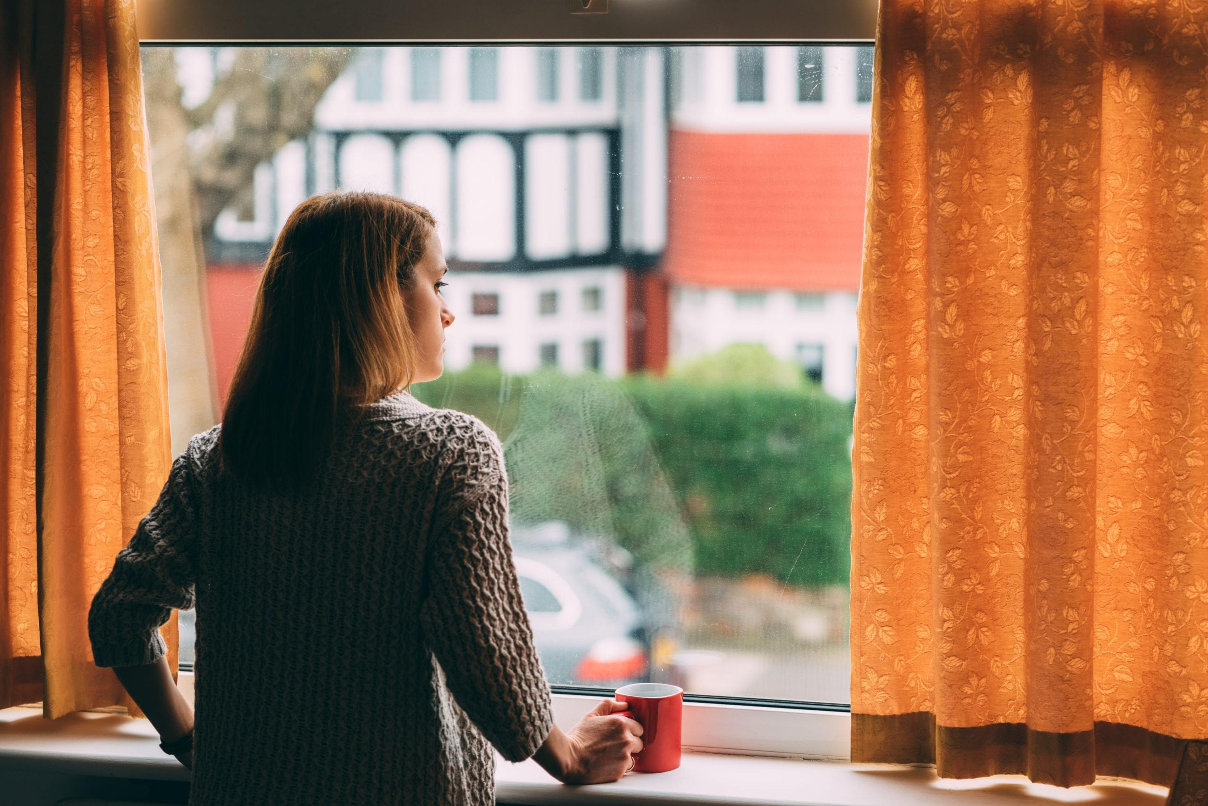 Woman staying home for safety during coronavirus pandemic and observing empty city