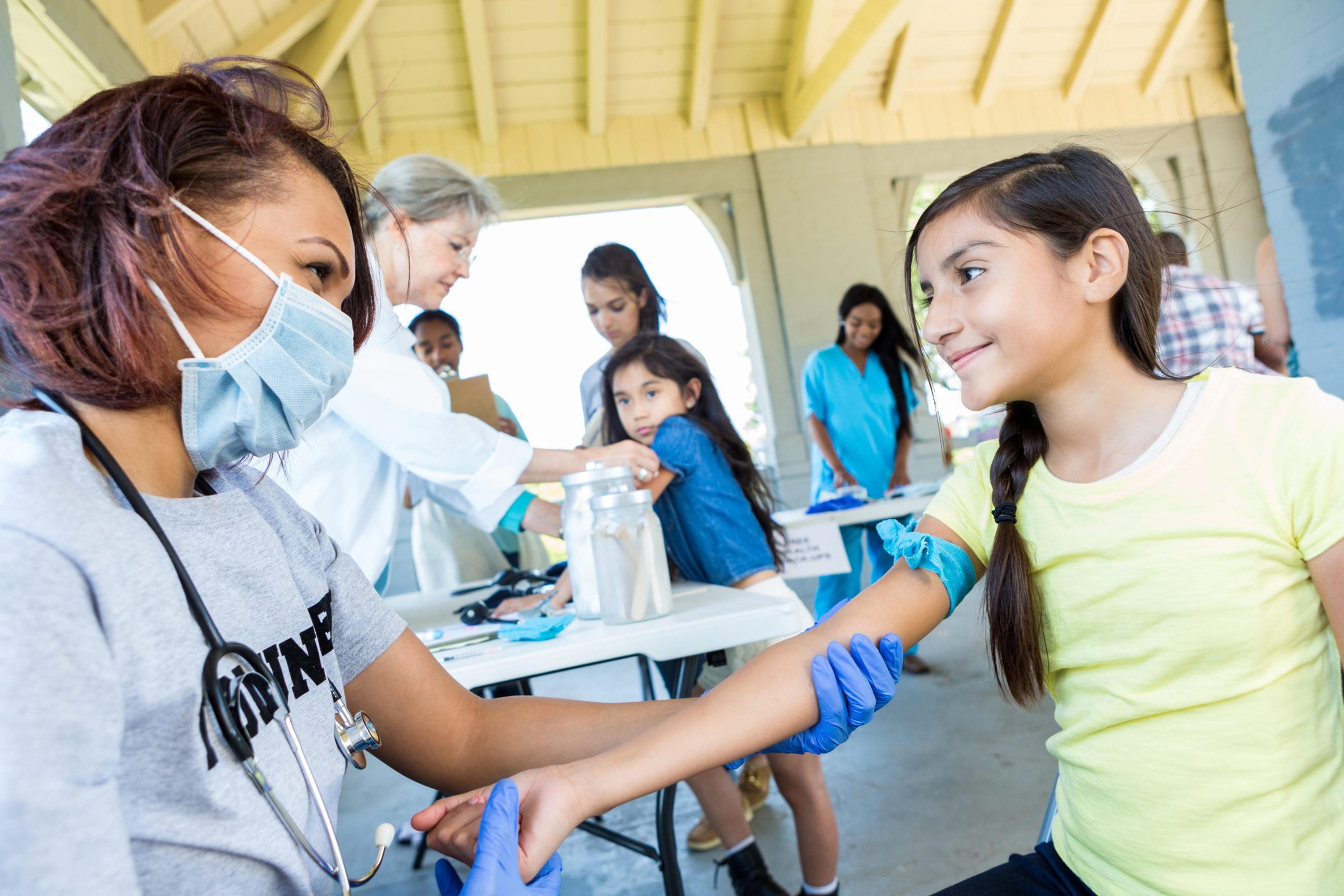 Volunteer doctor prepares to draw blood from a preteen girl