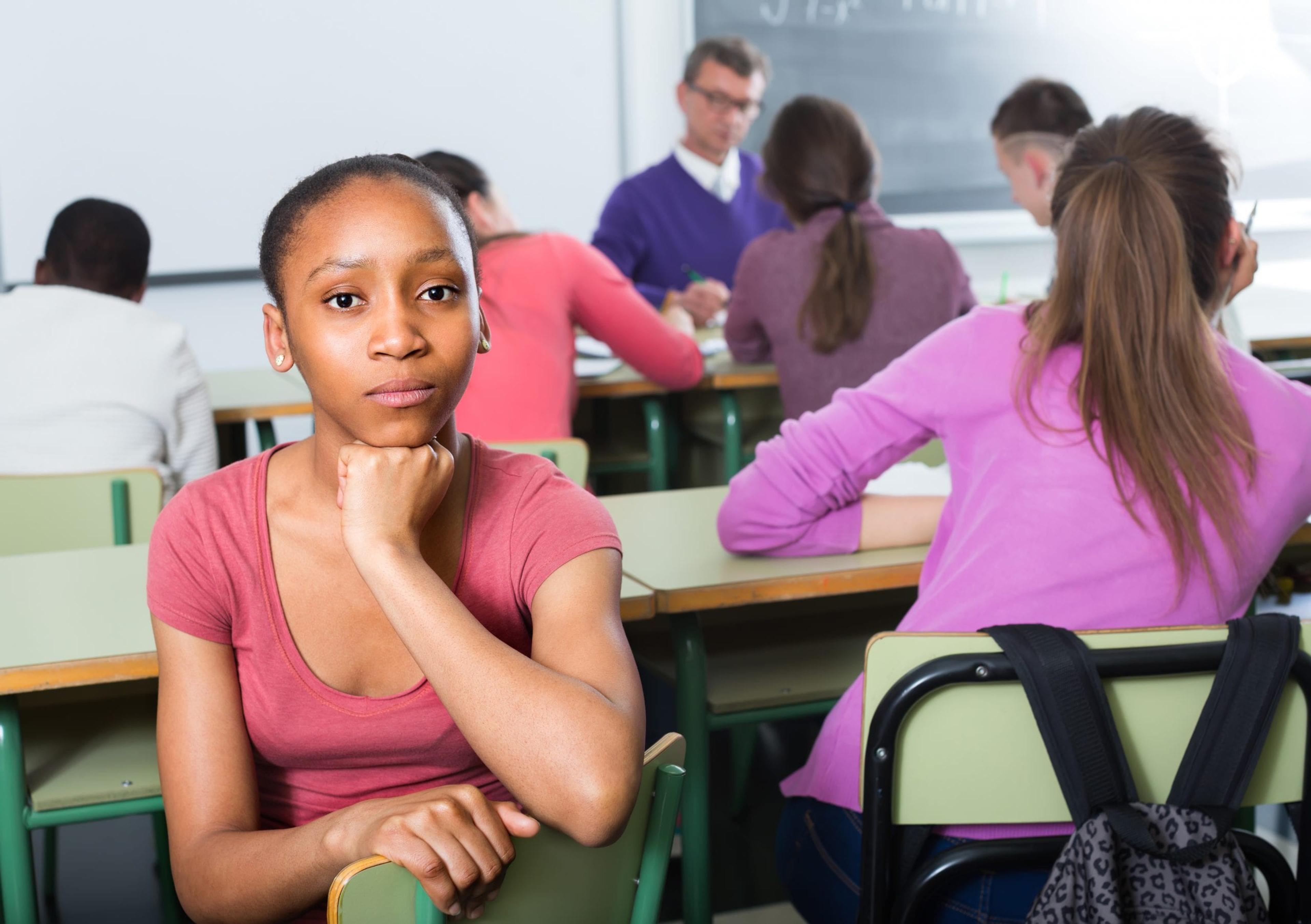 Portrait of a sad student girl sitting lonely while others listening the class