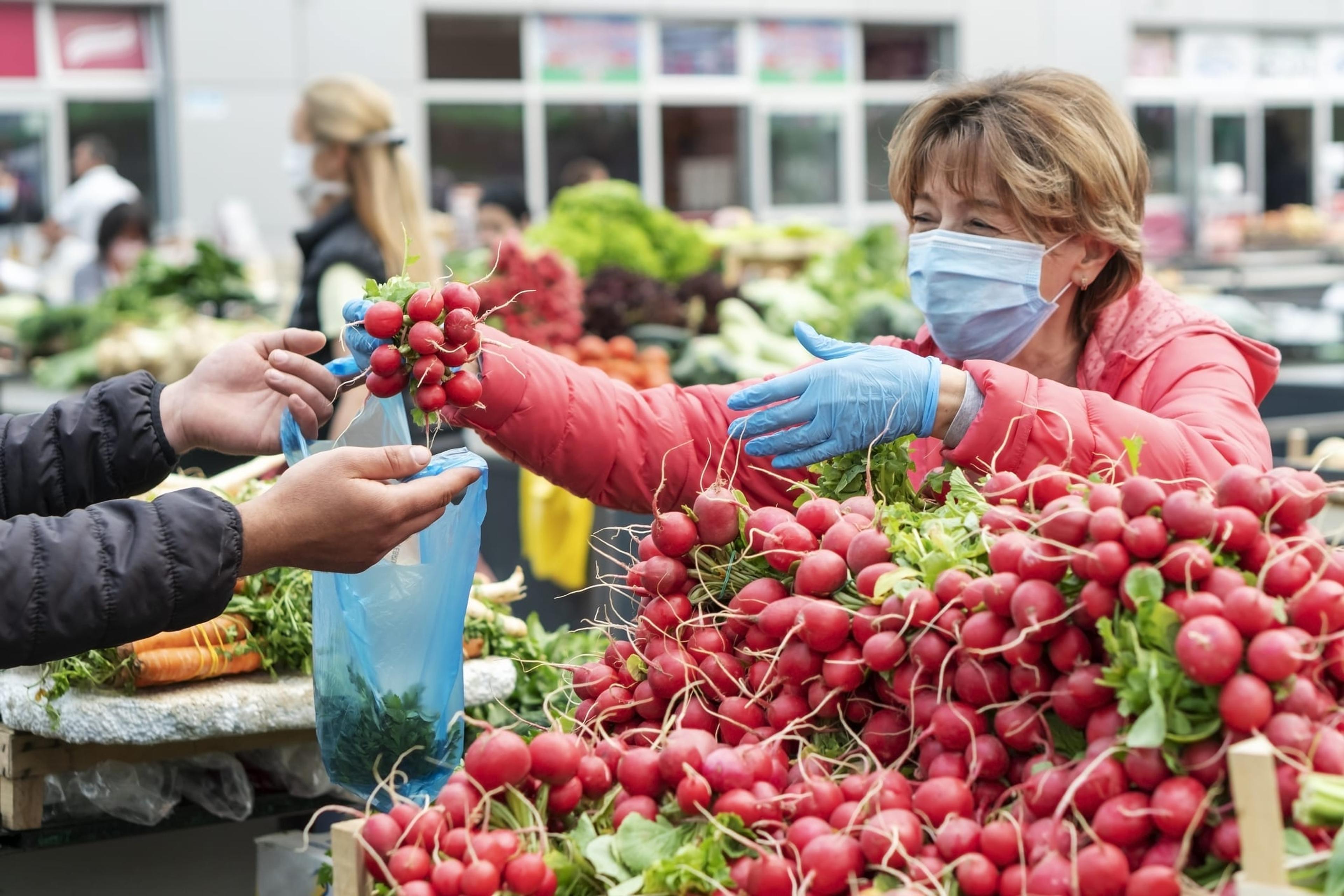Woman wearing a mask selling radishes at a farmers market