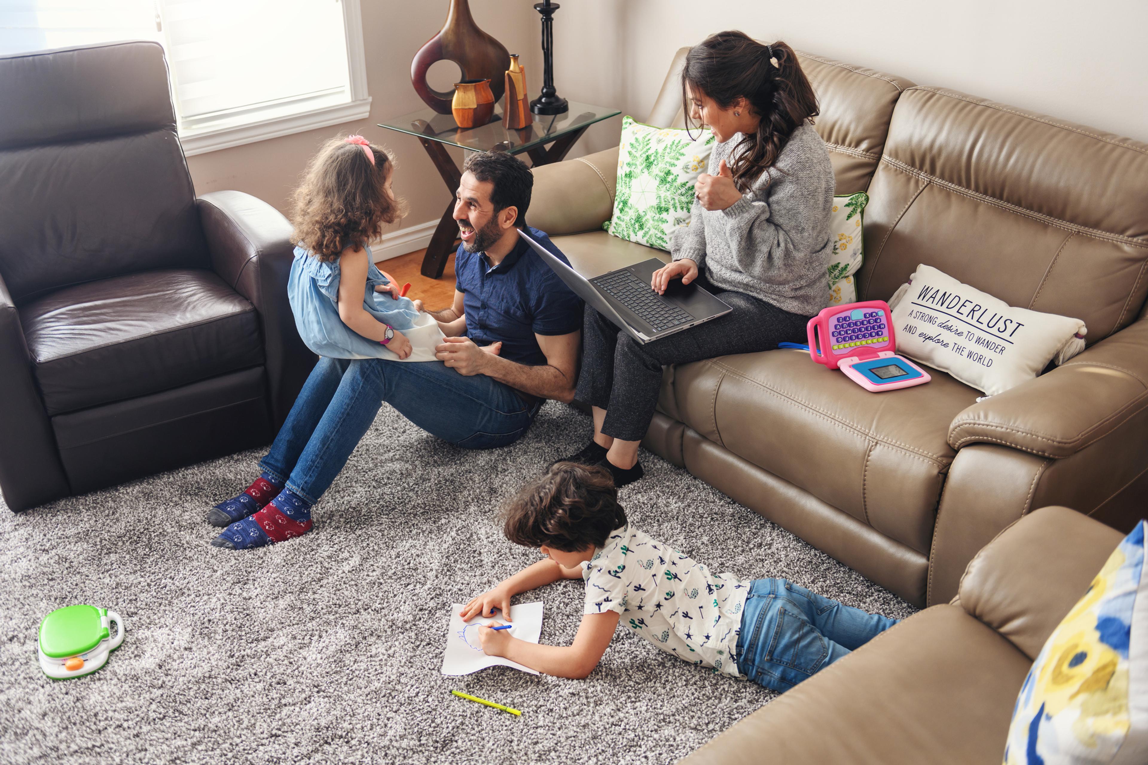 A family plays in the living room as a woman types on a computer.