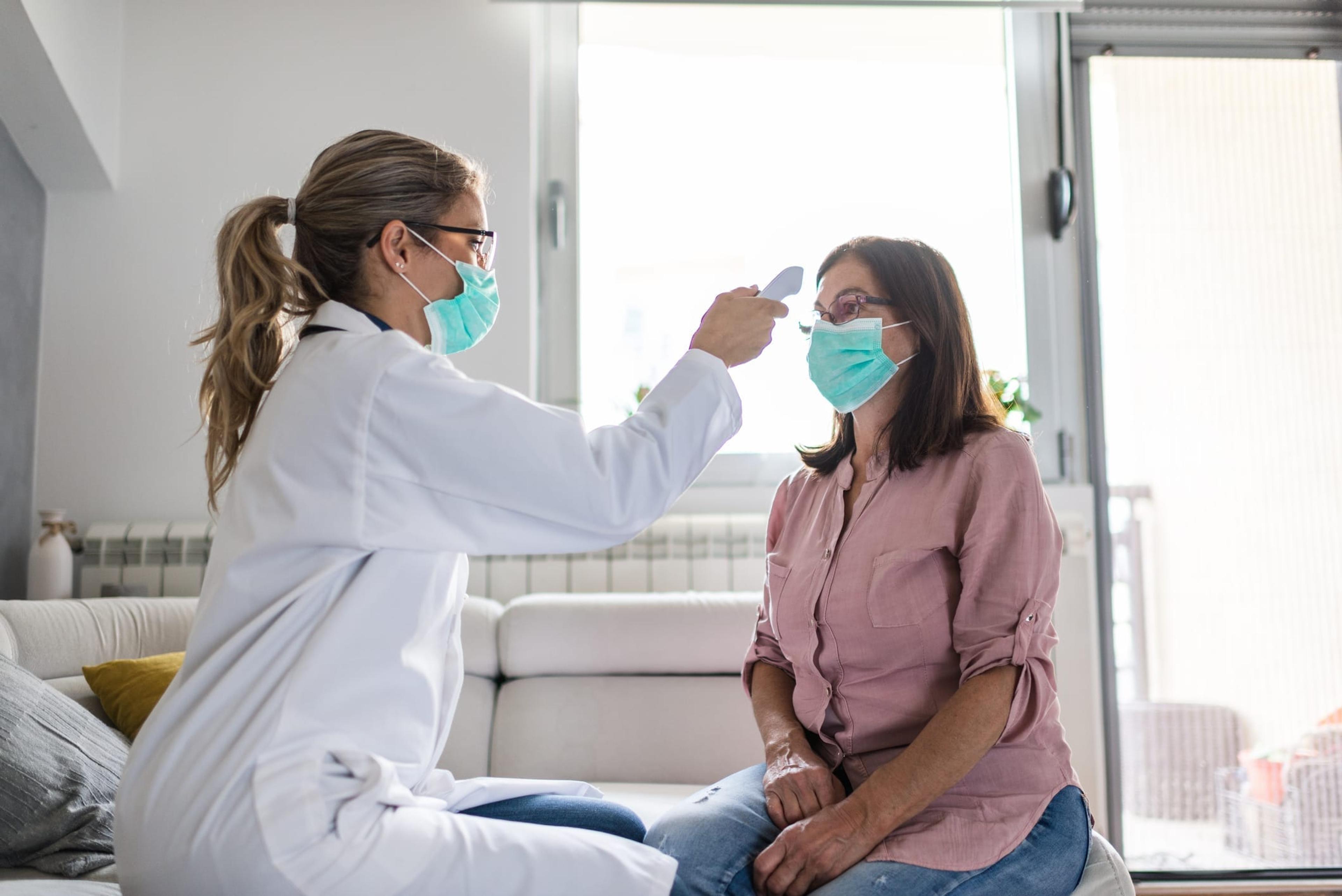 Healthcare worker at home visit. Female doctor is checking temperature to senior woman.