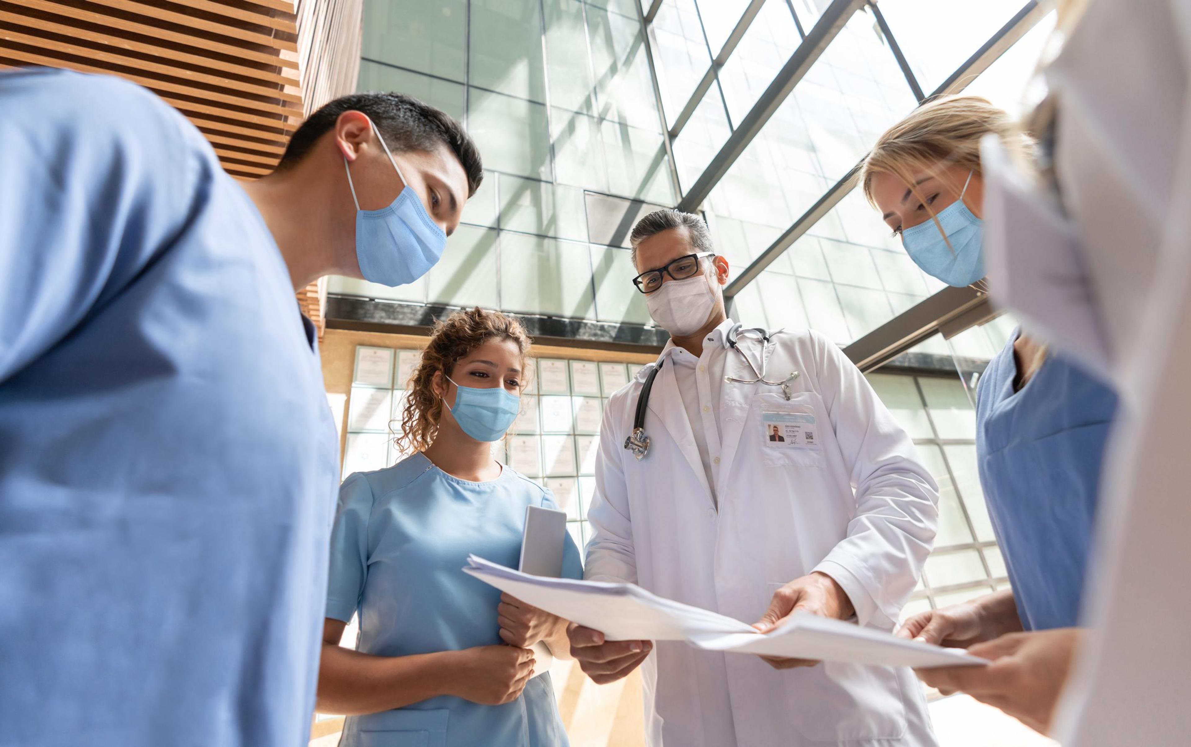 Group of doctors and nurses wearing masks gather for a meeting