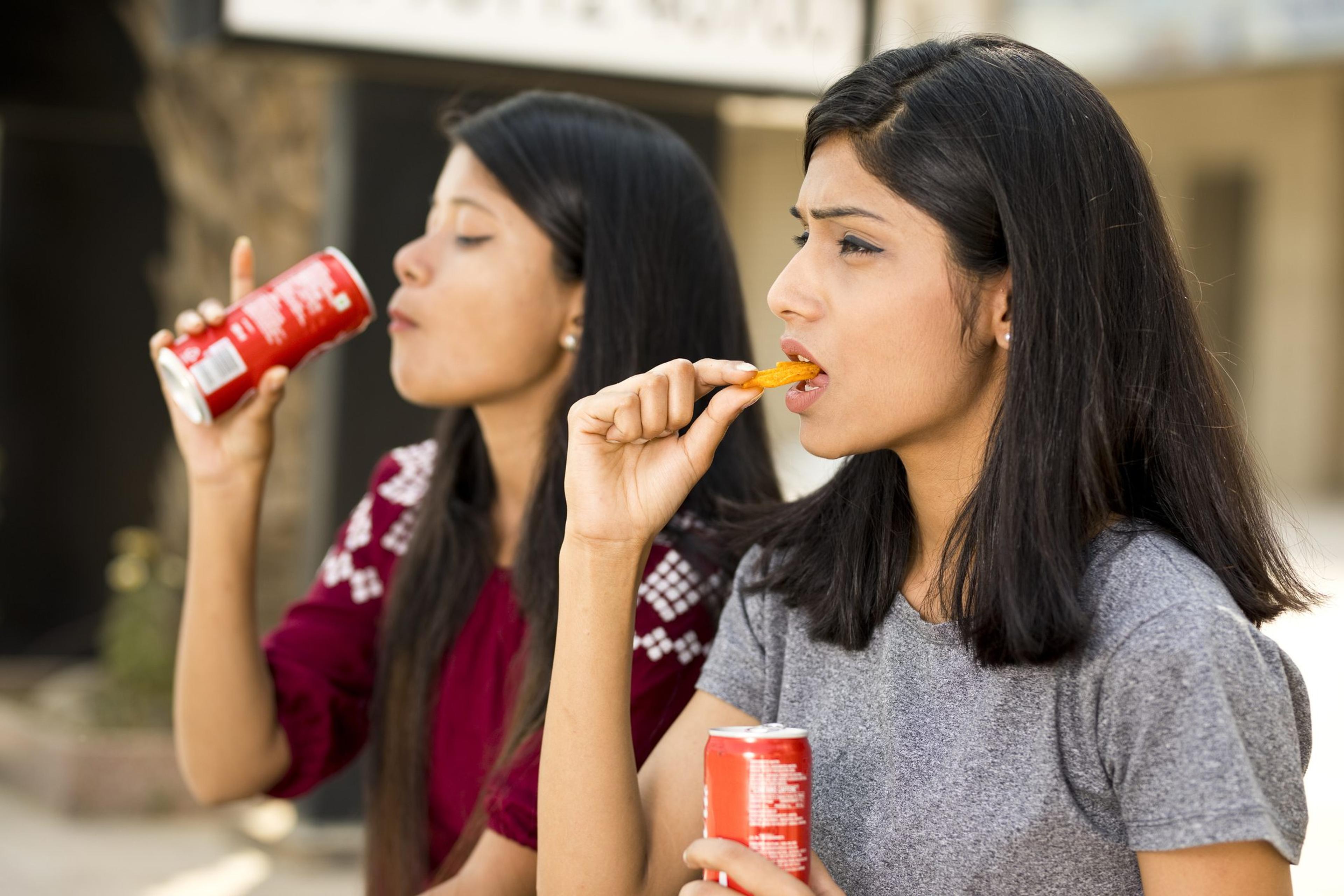 Young girls eating potato chips and holding pop can