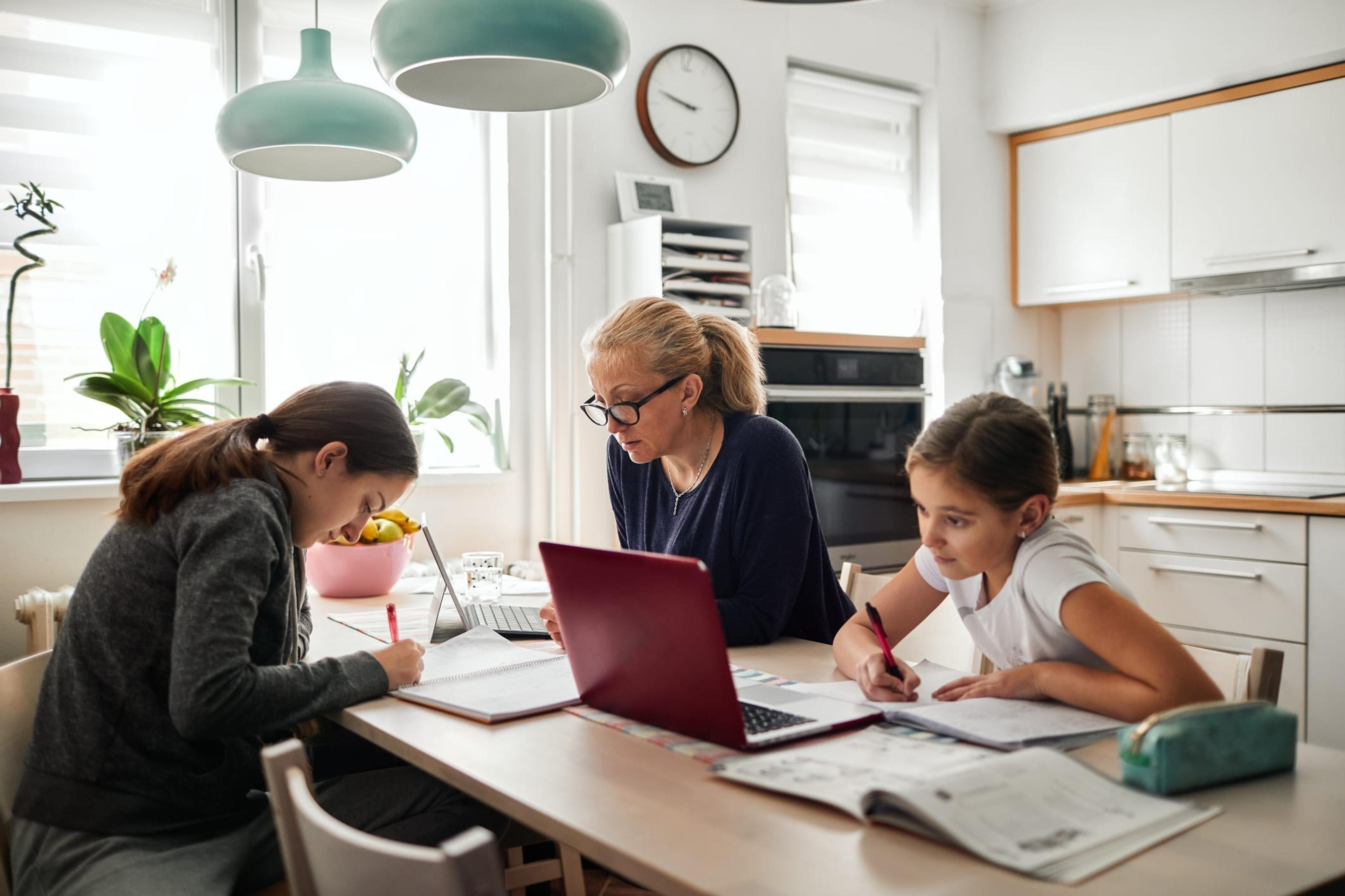 Mom helps two daughters with homework at kitchen table