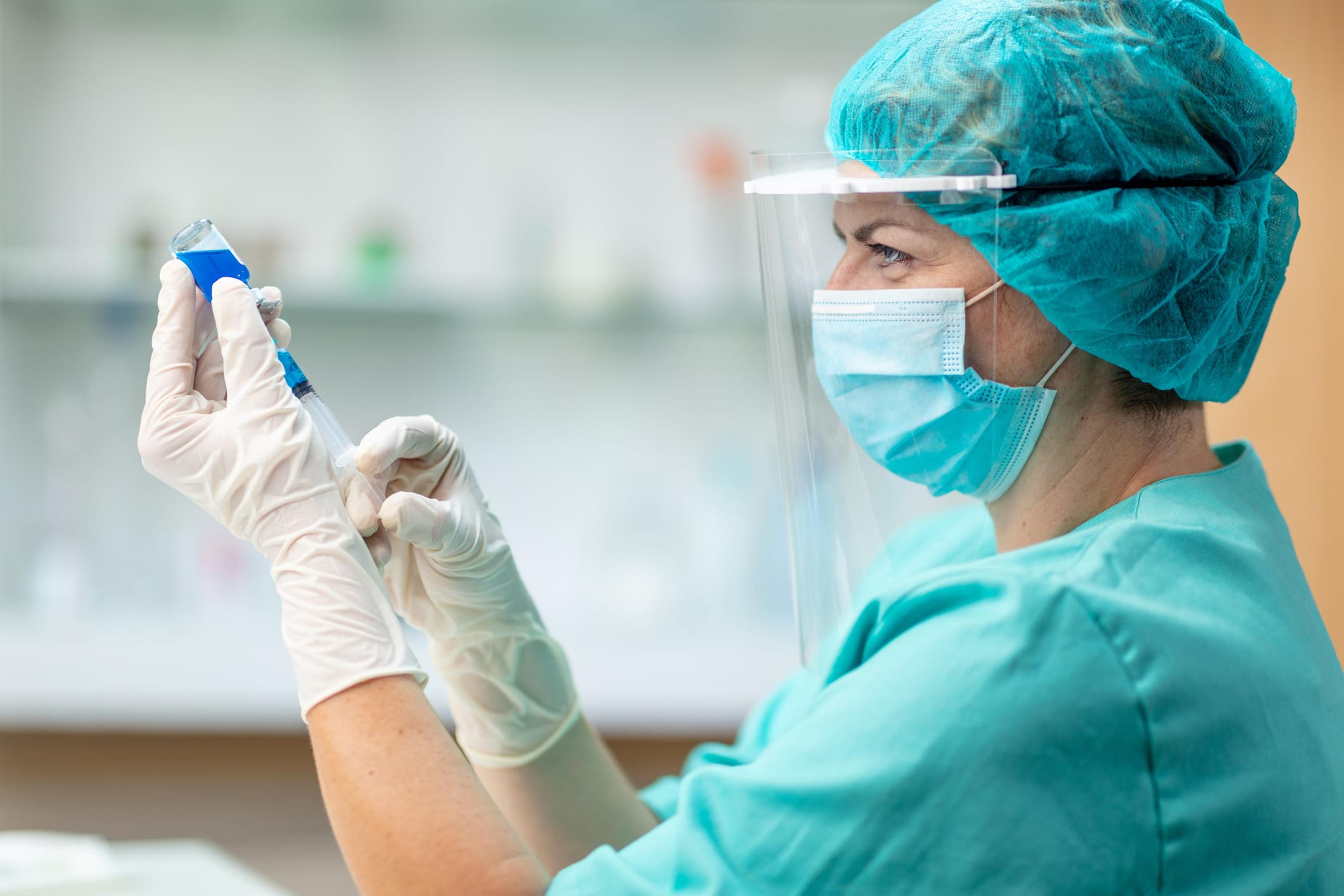 Female doctor wearing PPE and masks pulls vaccine from vial