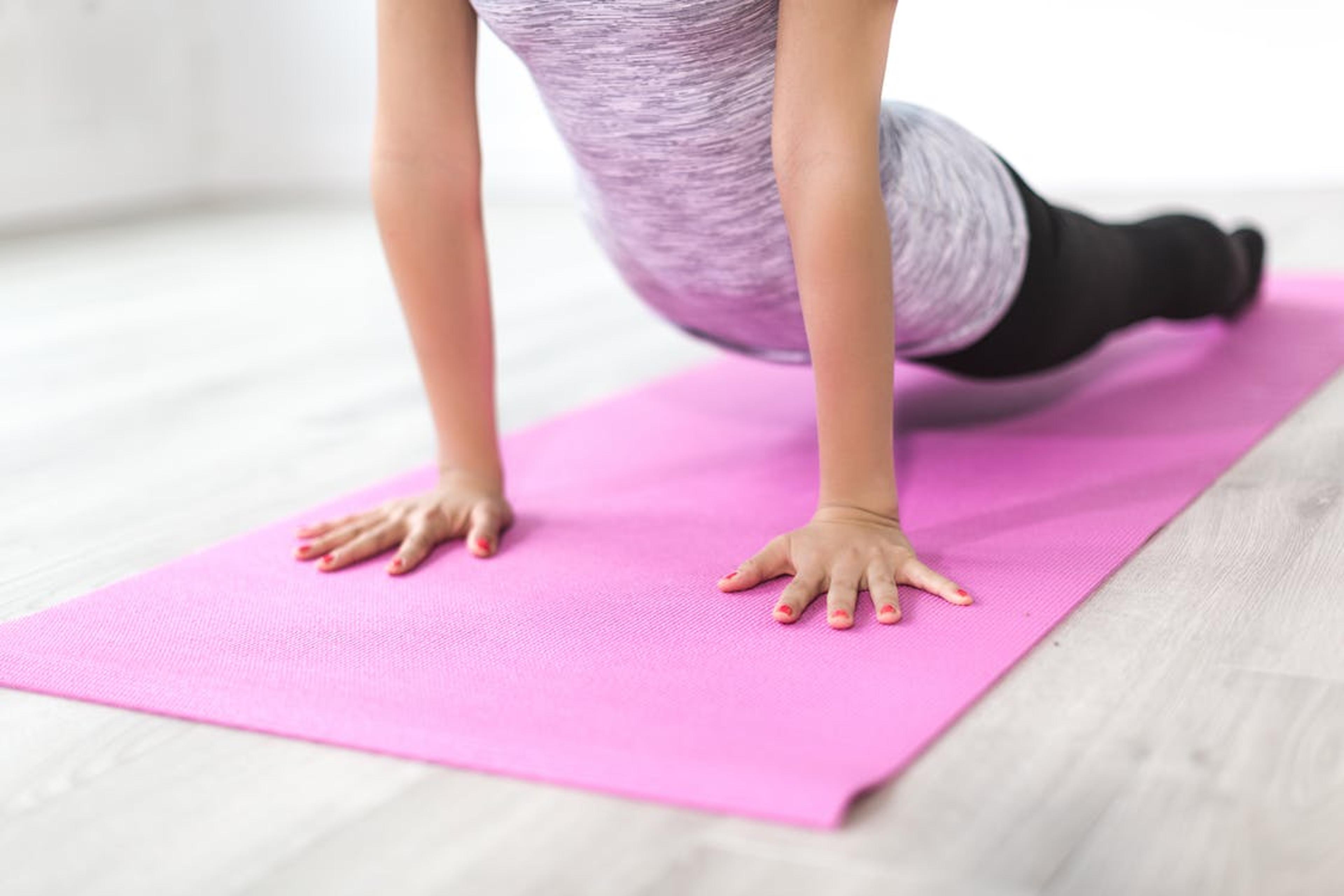 closeup of a woman with a pink yoga mat doing a yoga pose.