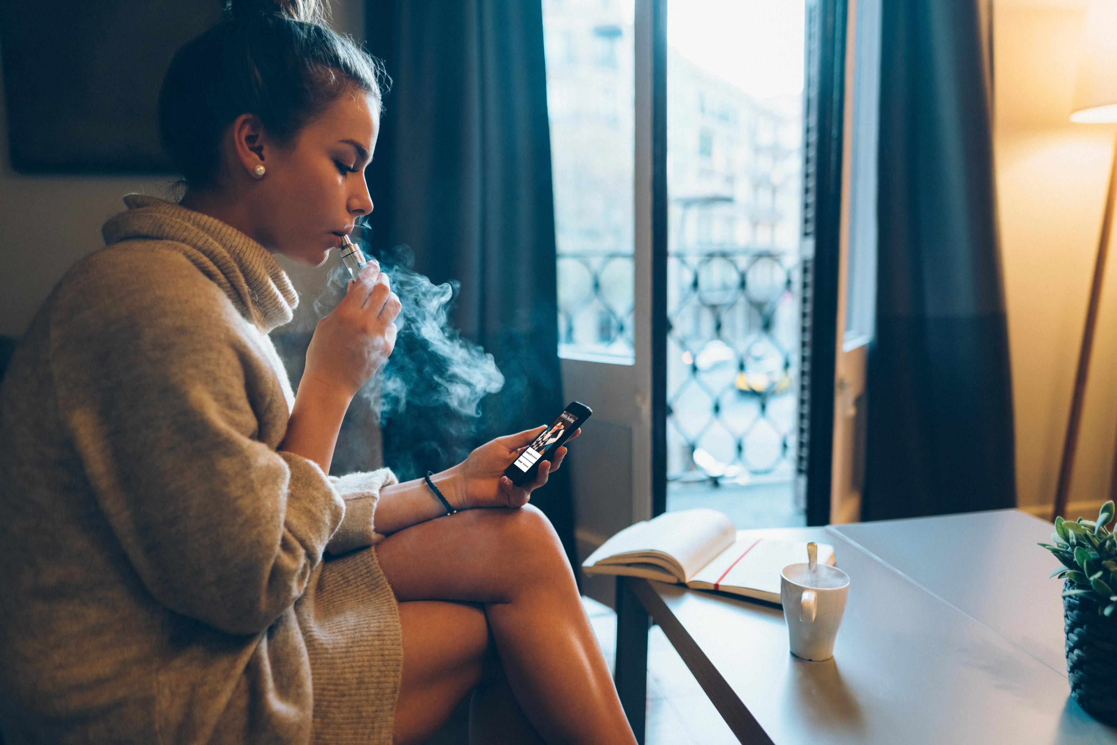 Woman vapes at home while sitting on the couch
