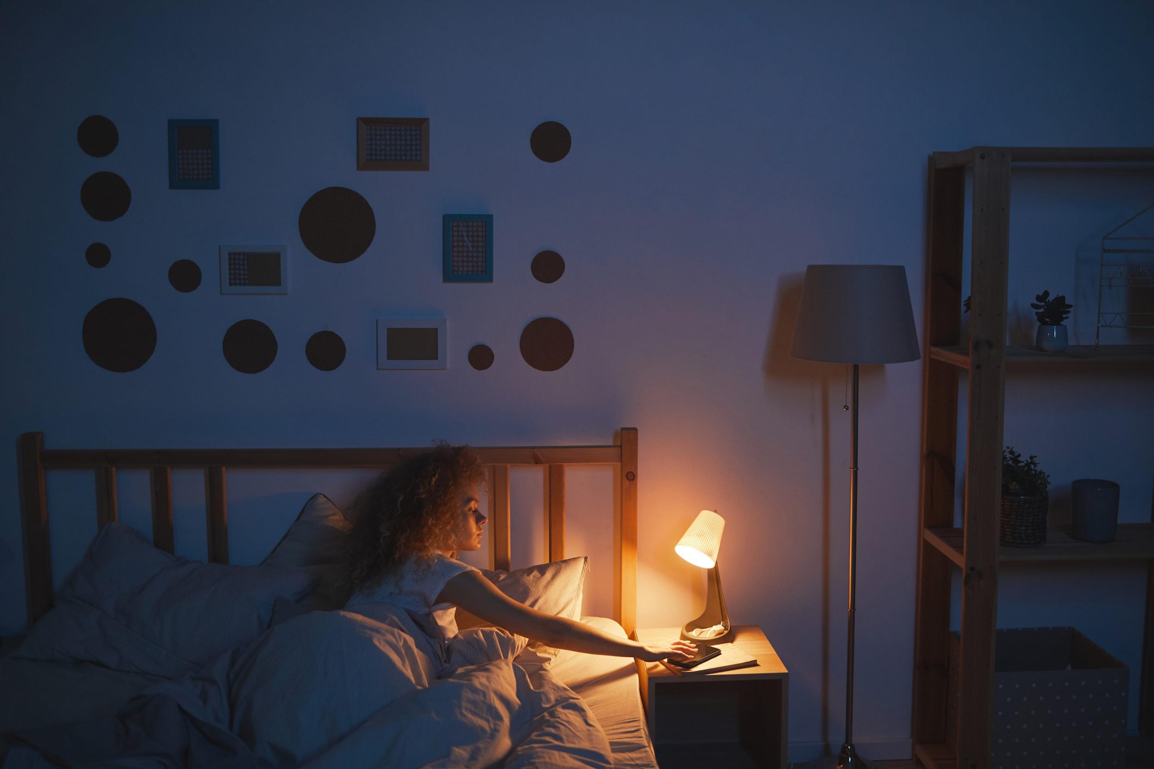 Young woman turning off her bedside lamp at nighttime