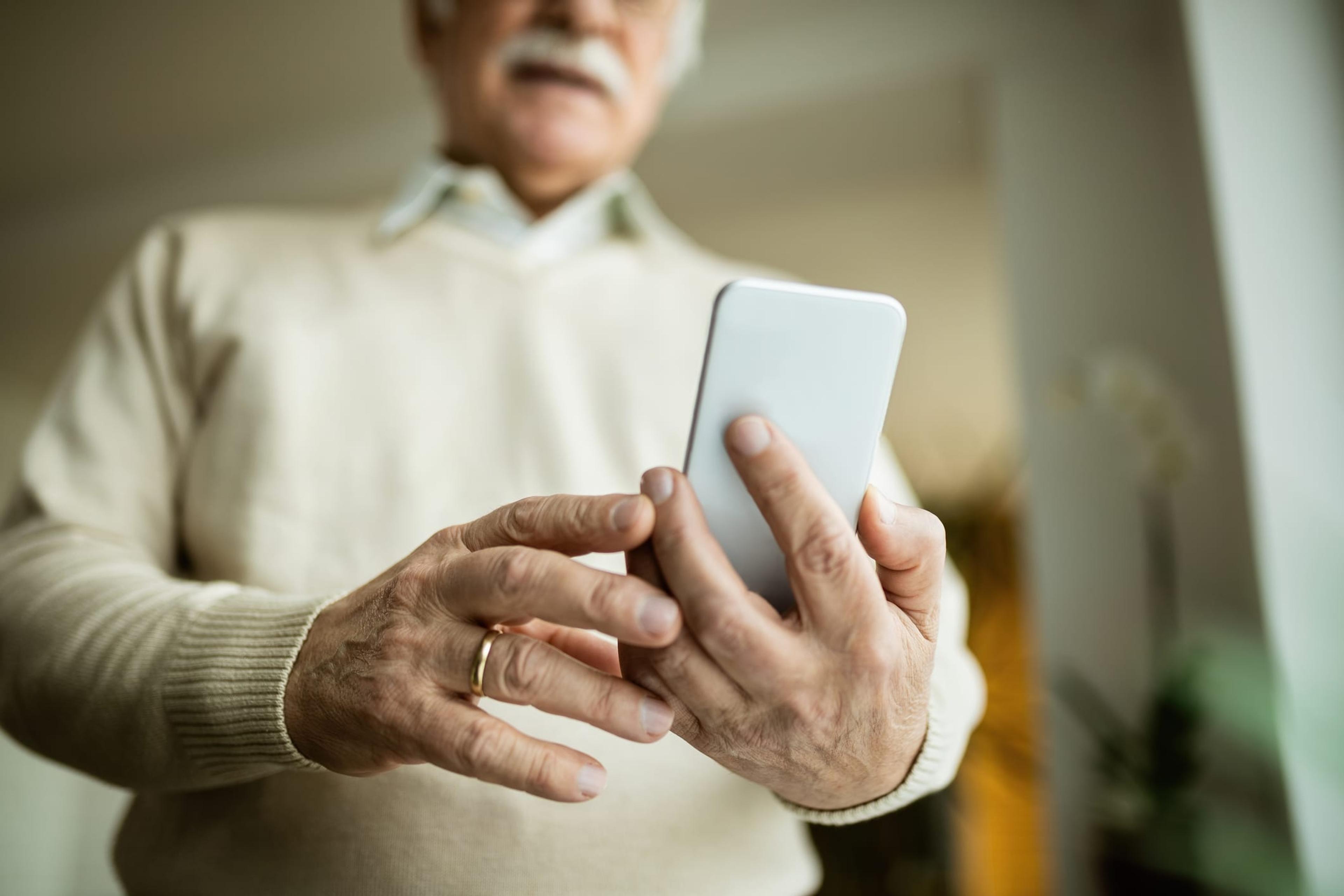 Older man holds an iPhone 12 in his hands away from his chest