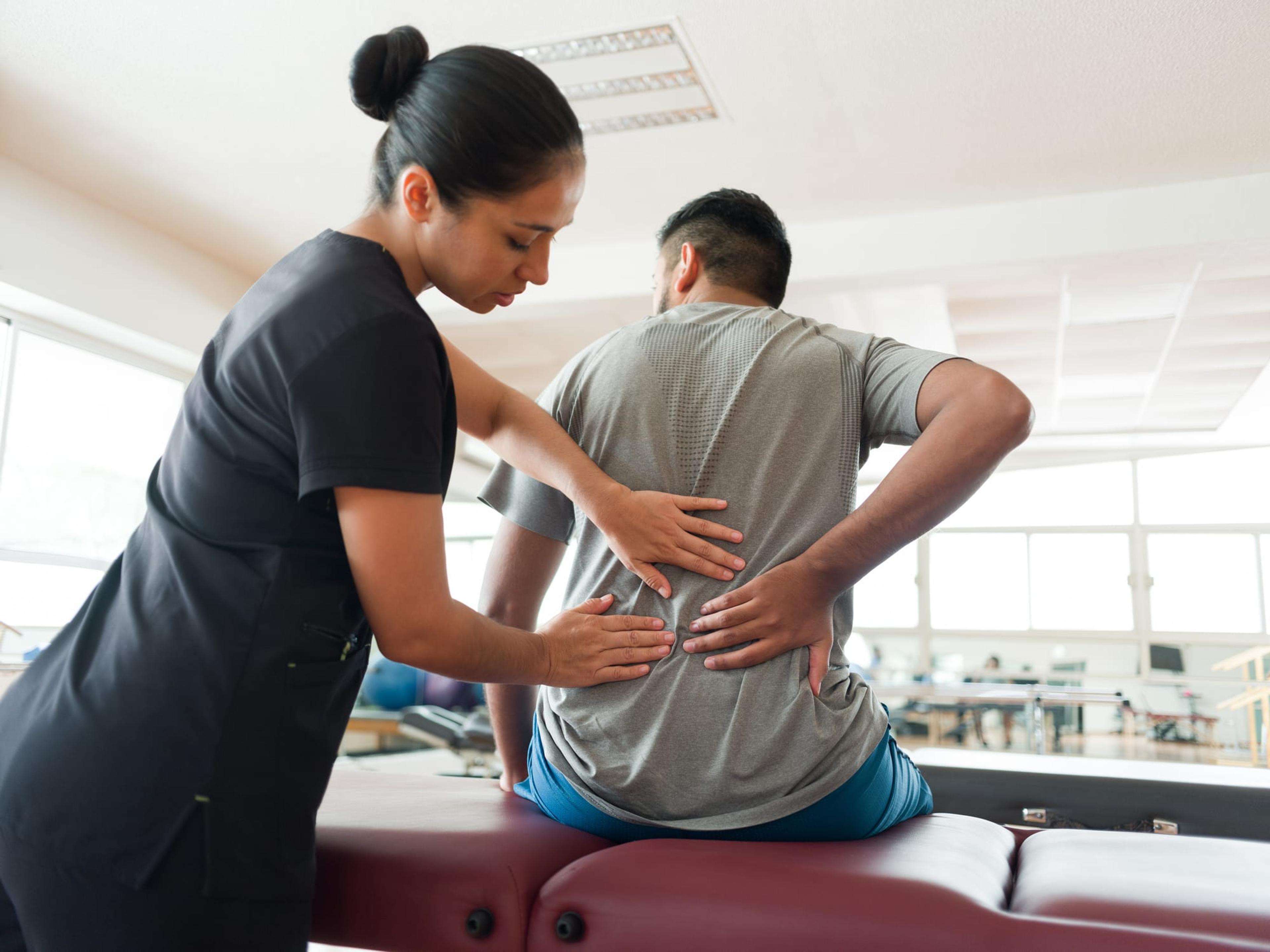 Female therapist helps a man with his back pain