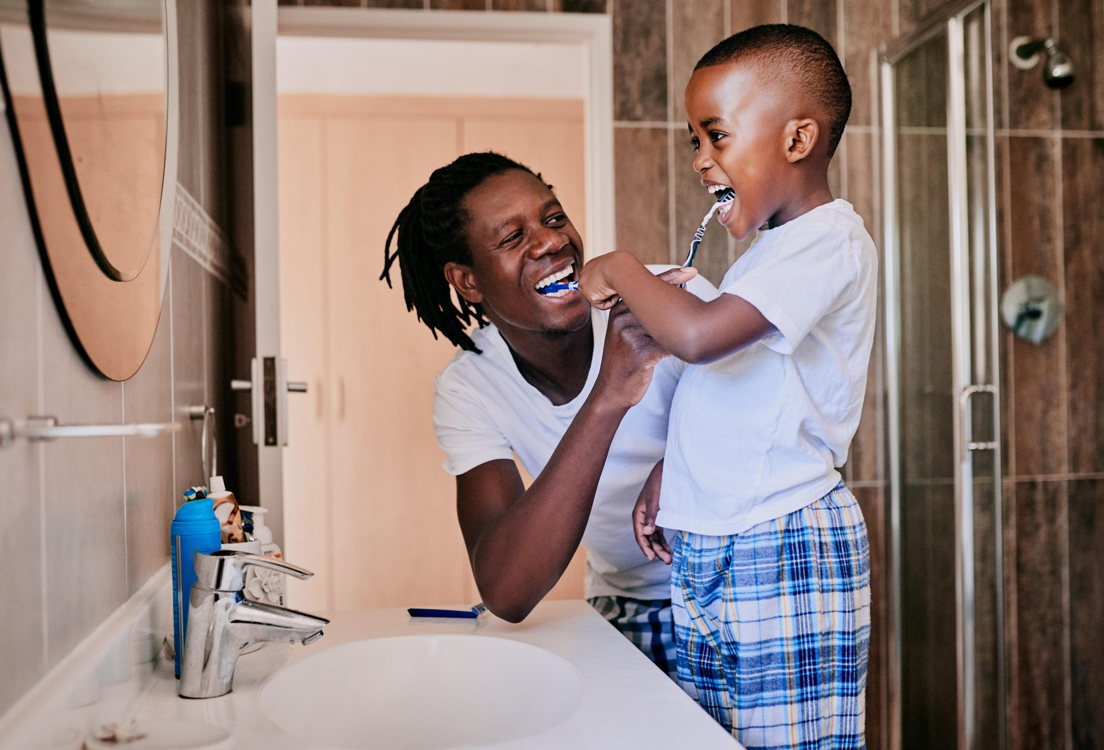 Father helps his son brush his teeth teaching good dental habits to children
