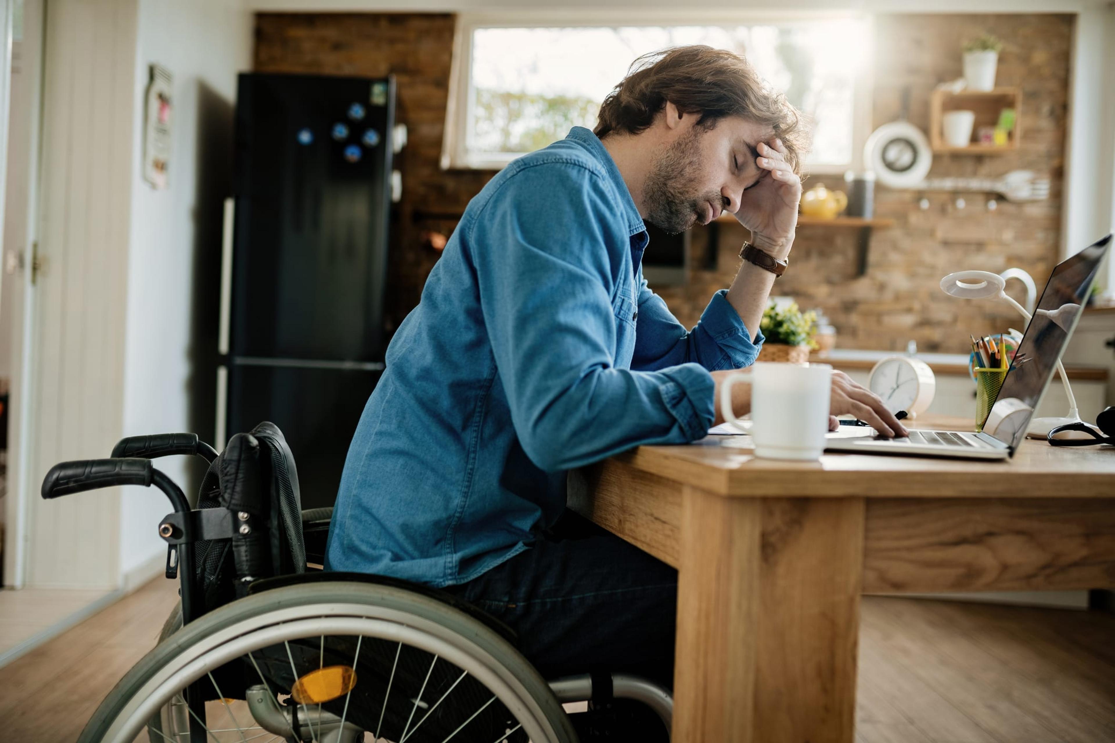 Man in a wheelchair appears stressed at his kitchen table