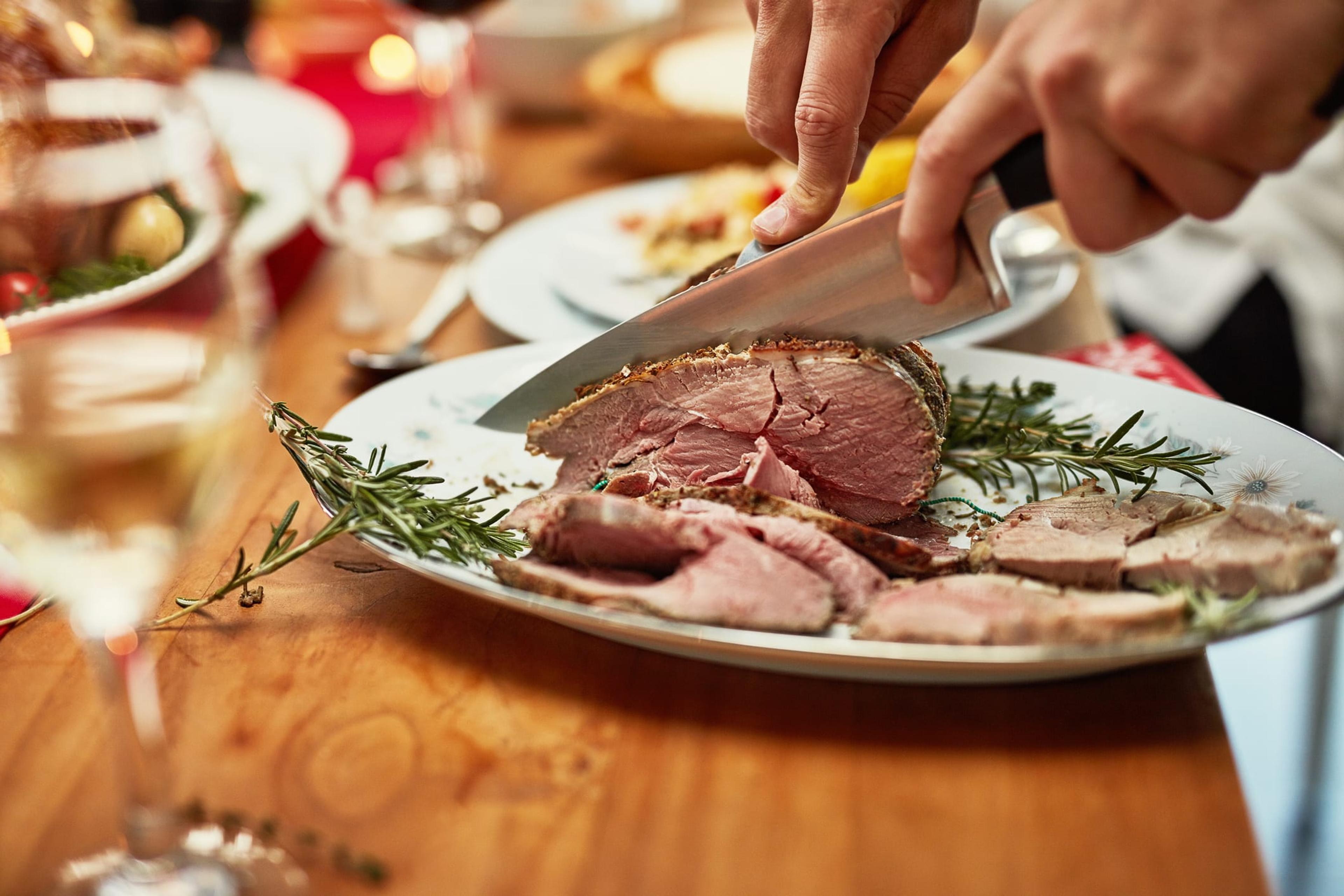 A hand slicing a piece of beef at dinner