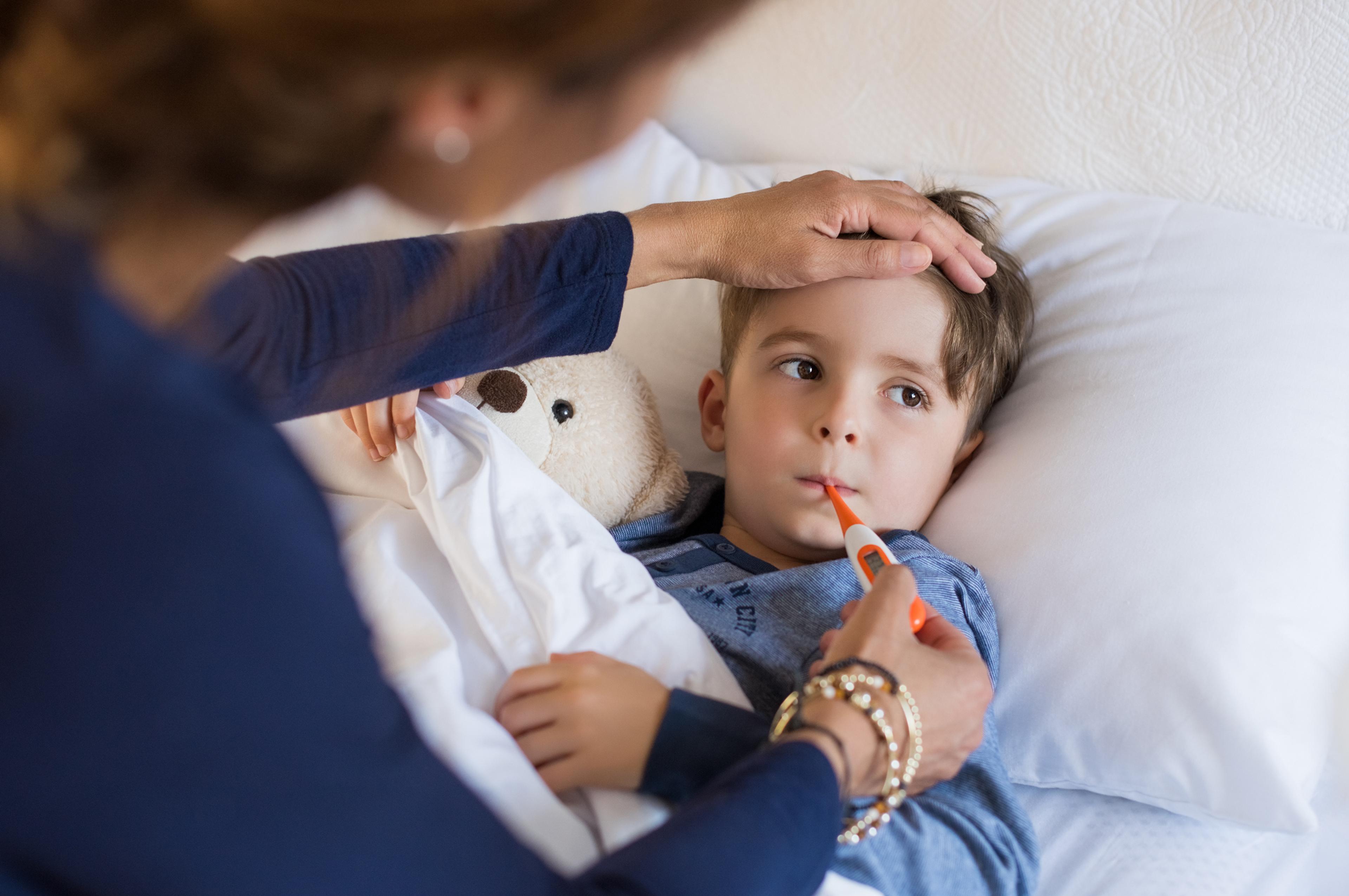 A young boy has his temperature checked in bed.