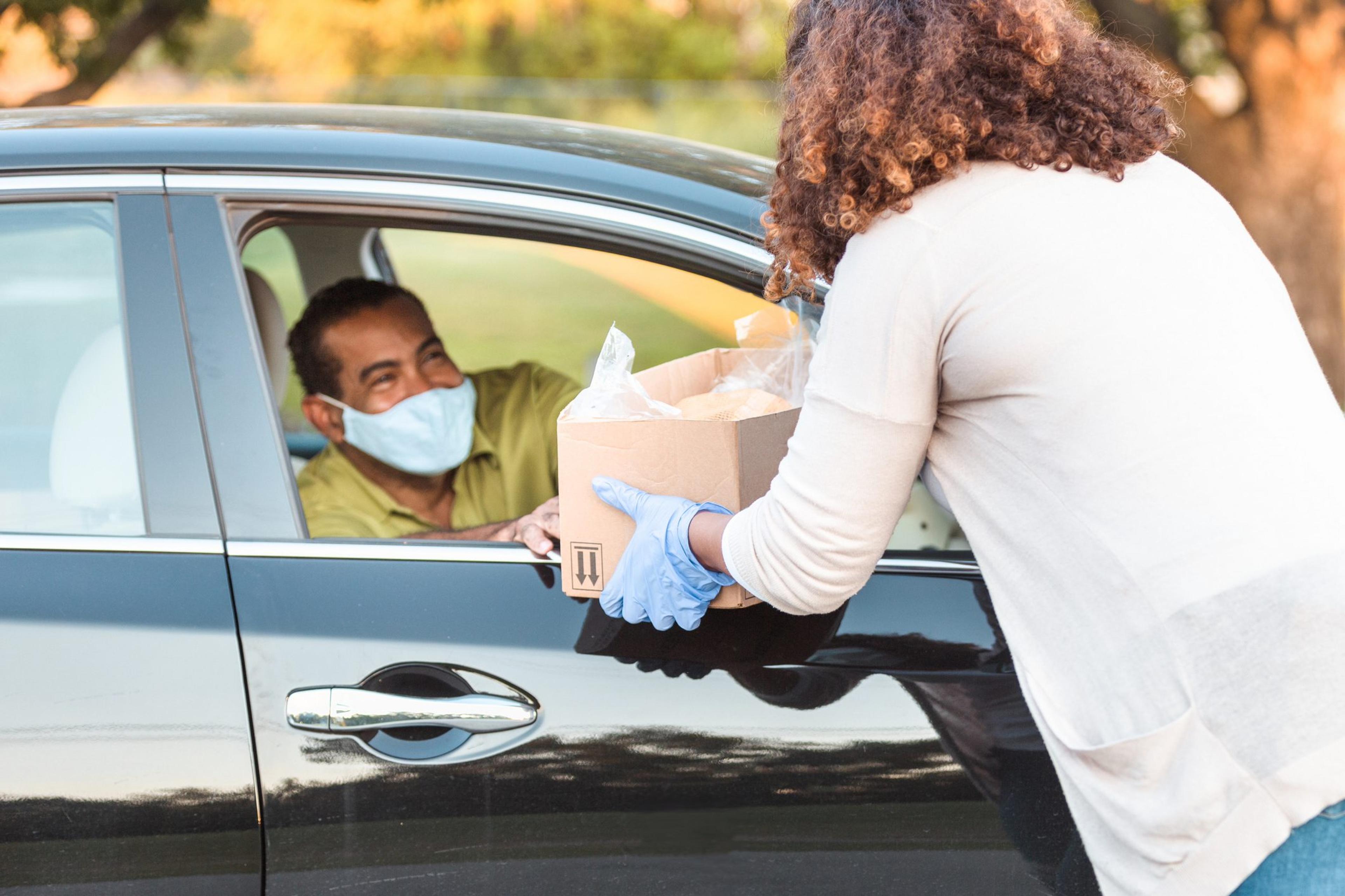 Man wearing a mask driving his car receives a bag of food