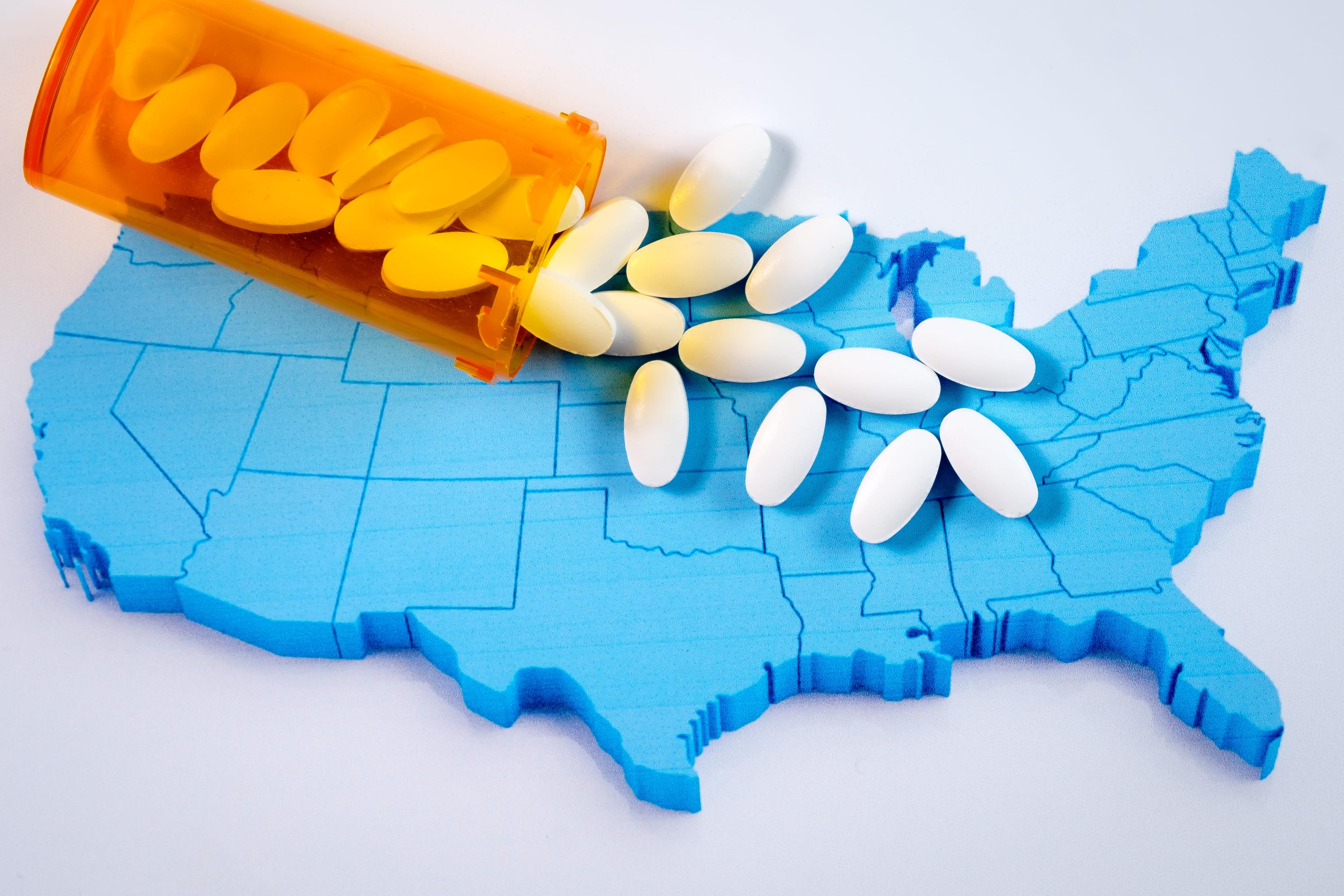 White pharmaceutical pills spilling from prescription bottle over American map.
