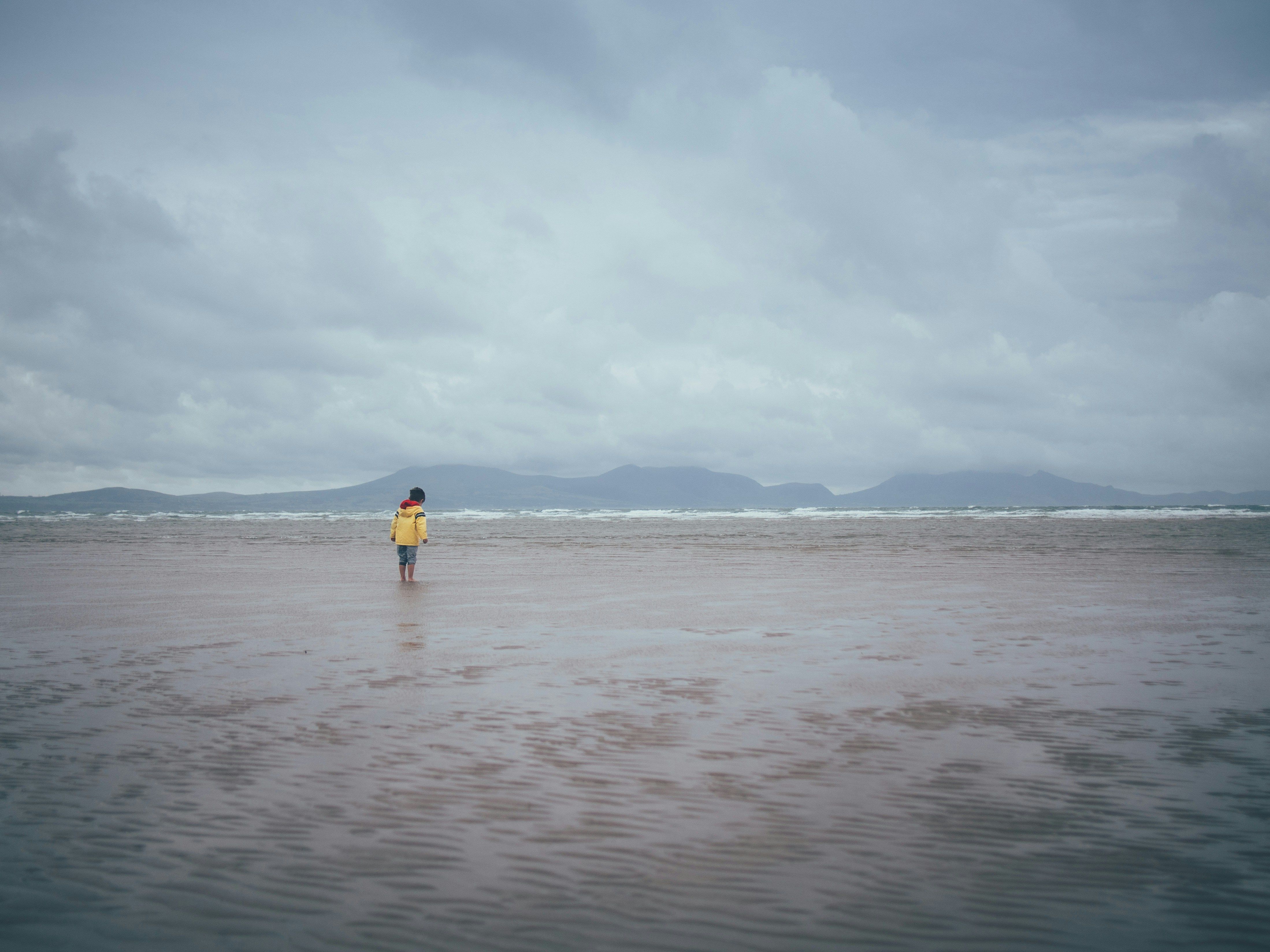 child in raincoat with feet in sand 