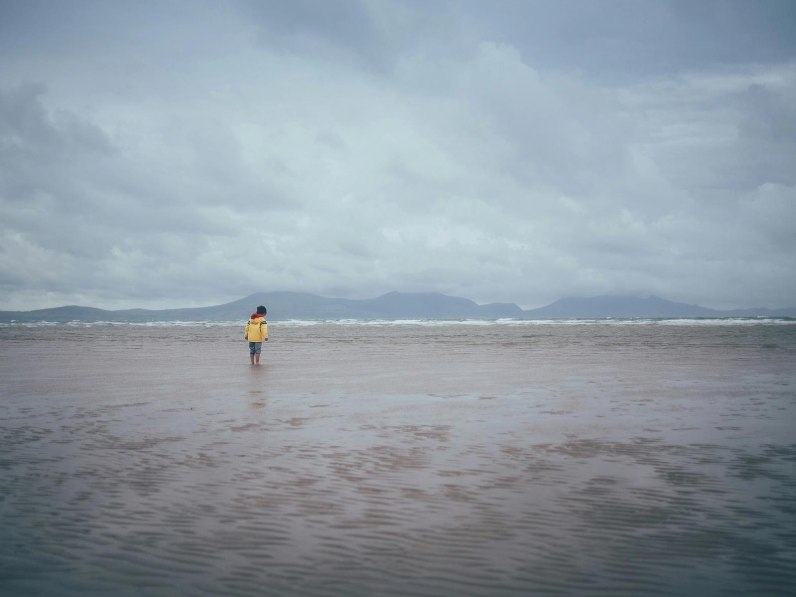 child in raincoat with feet in sand 