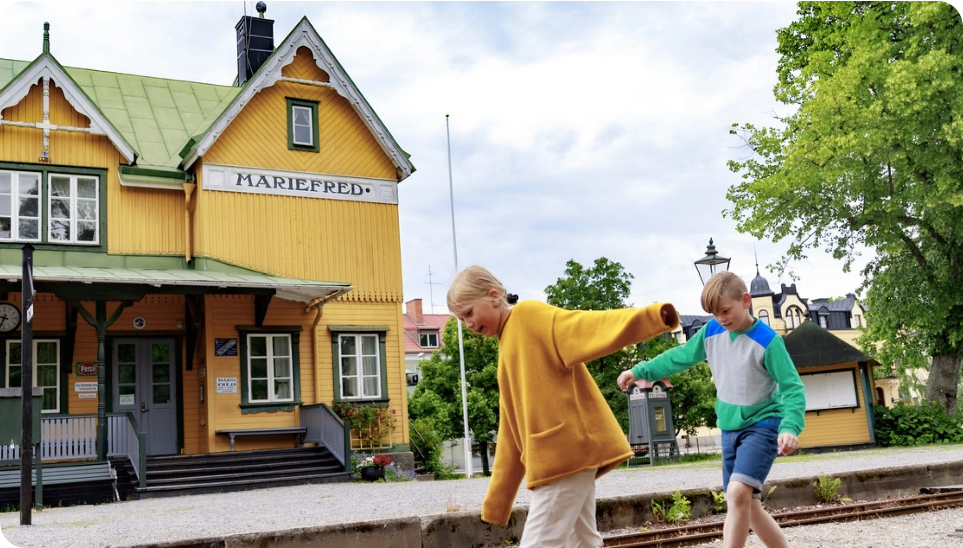 Två barn går balansgång utanför stationshuset i Mariefred.