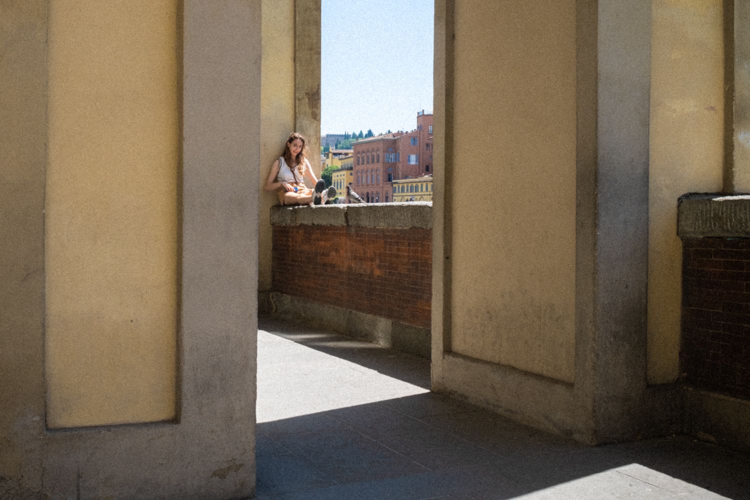 Eine junge Frau sitzt in den Arkaden am Ufer des Arno in Florenz. Sie schaut ins Bild und lächelt.