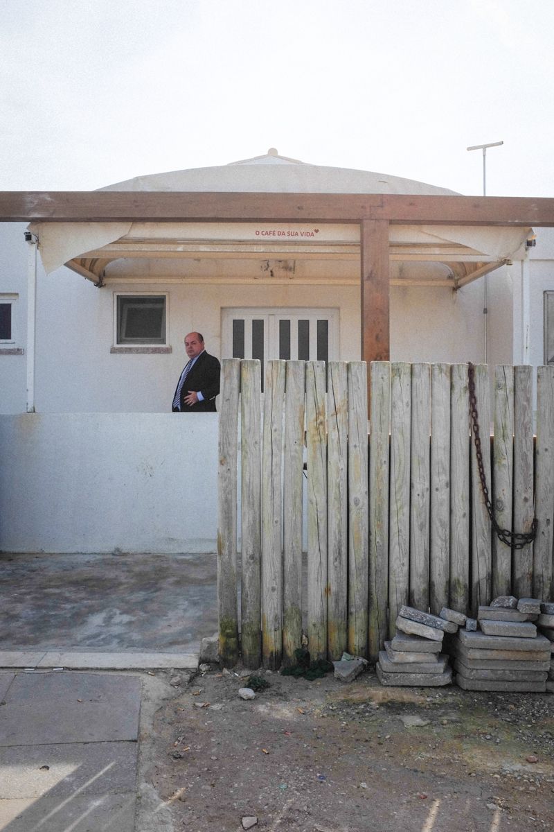Straßenfotografie mit Strandhaus in einem Vorort von Lissabon. Ein Mann verlässt das Gebäude und blickt in die Kamera.