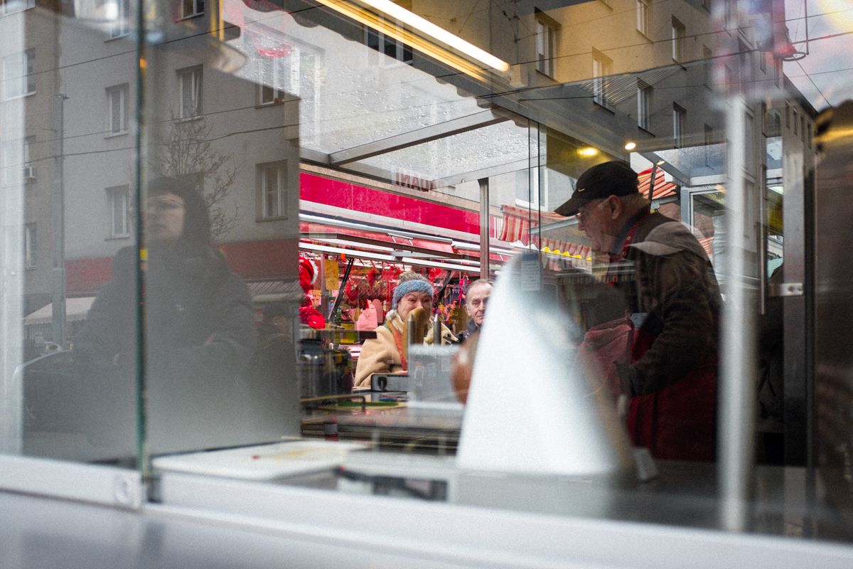 Straßenfotografie auf einem Wochenmarkt in Wien. An einem Imbiss kaufen Menschen Snacks.