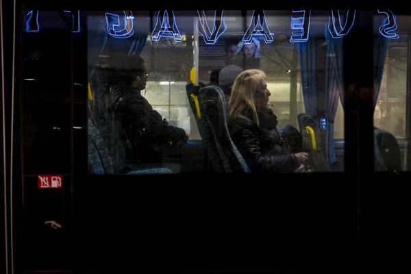 Street Photography Stockholm Street Photography Stockholm - Eine Frau sitzt in der Nacht in einem Bus, auf dessen Scheiben sich Leuchtreklamen spiegeln.