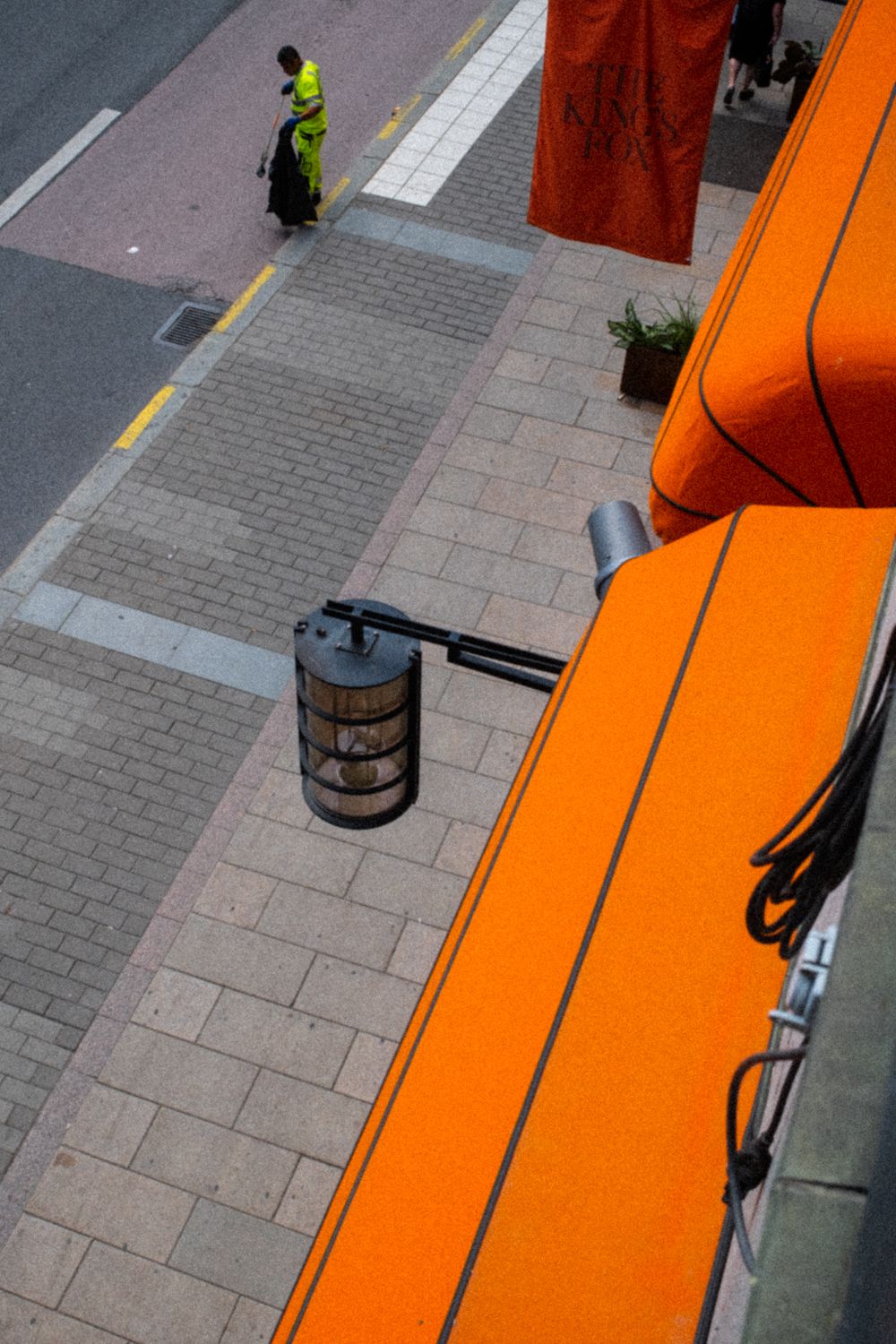 Blick über orangenfarbene Markise auf einen Gehweg in der Stockholmer Innenstadt. Straßenreinigung findet gerade statt.