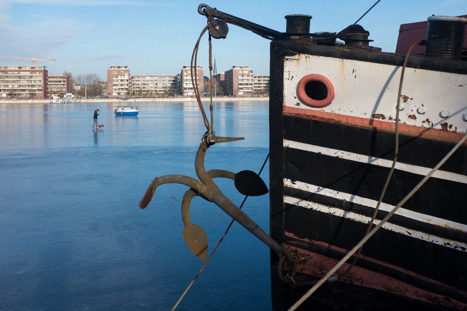 Zugefrorene Spree in der Rummelsburger Bucht Berlin. Ein Mann spaziert auf dem Eis. Im Vordergrund ein altes Boot. Street Photography berlin