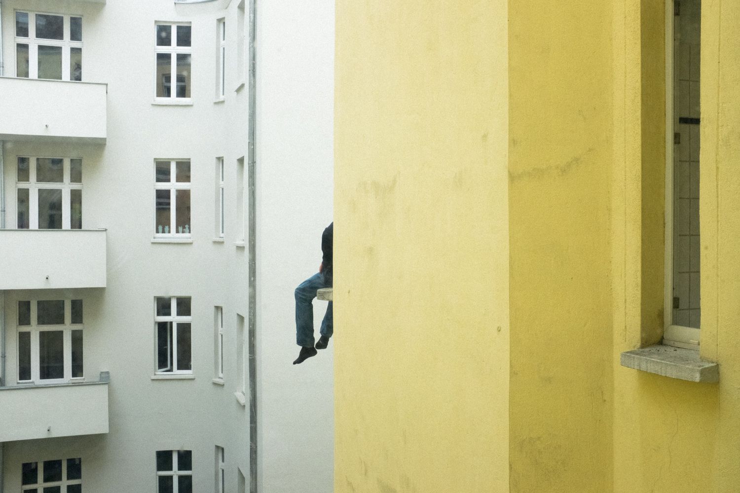 Mann sitzt auf dem Fensterbrett in einem Berliner Hinterhof.