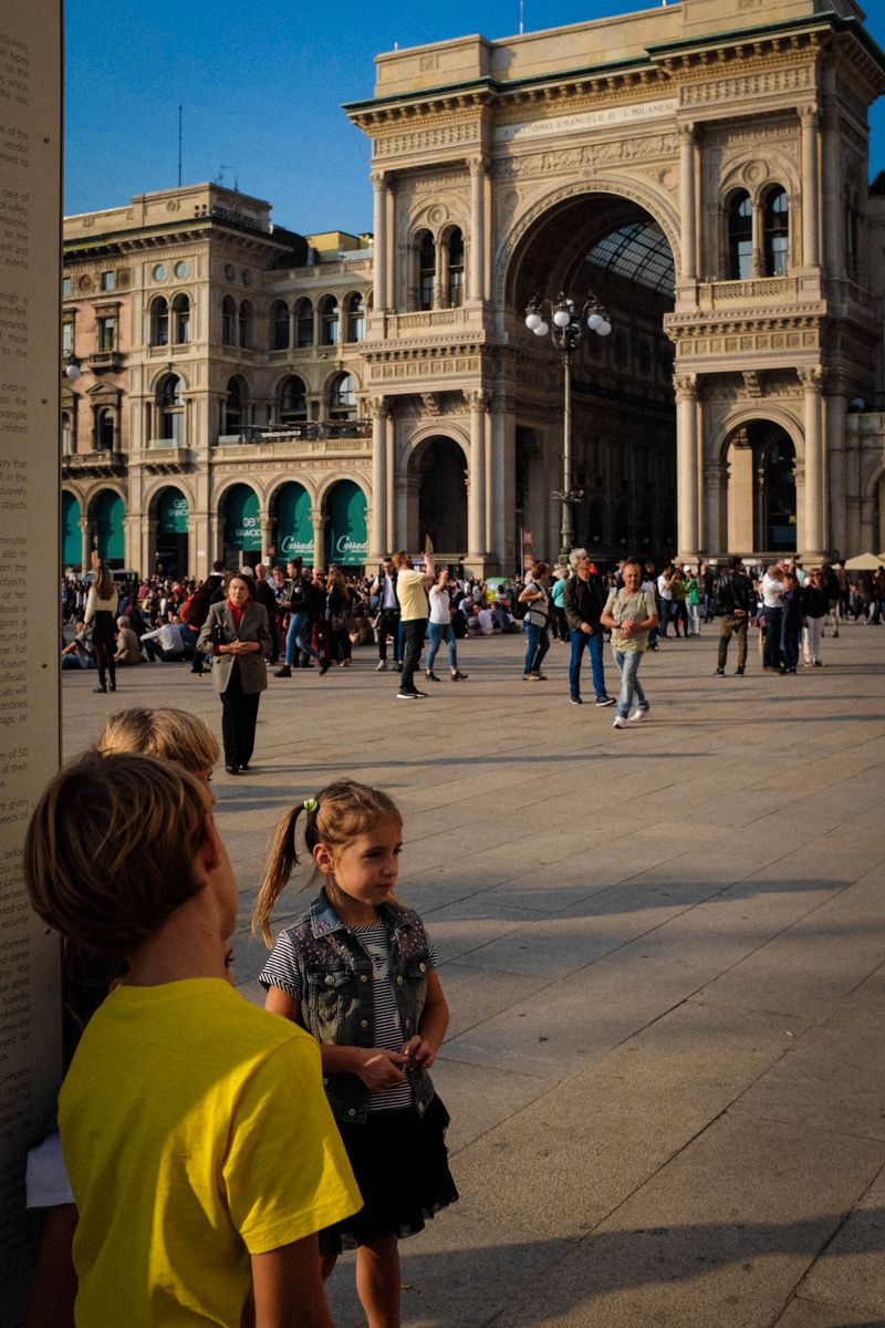 Kinder spielen auf dem Mailänder Domplatz, der Piazza del Duomo. Im Hintergrund ist der Eingang zur Galleria Vittorio Emanuele II zu sehen, der bekanntesten, überdachten Einkaufspassage Mailands.