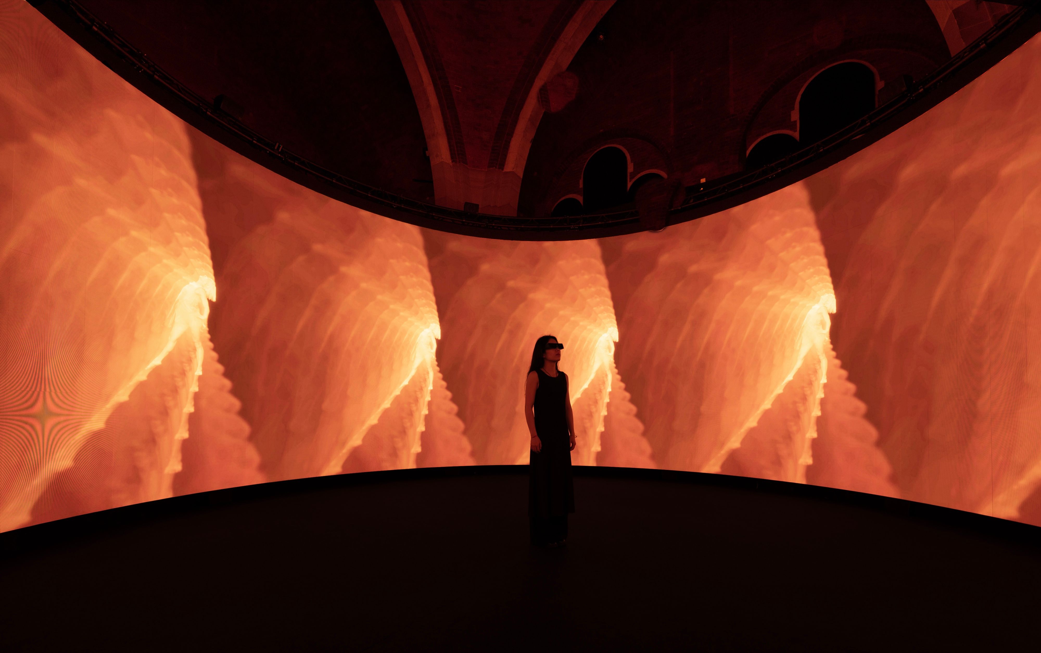 A visitor in 3D glasses inside the screen, surrounded by orange imagery, Wayne McGregor, On The Other Earth, Stone Nest