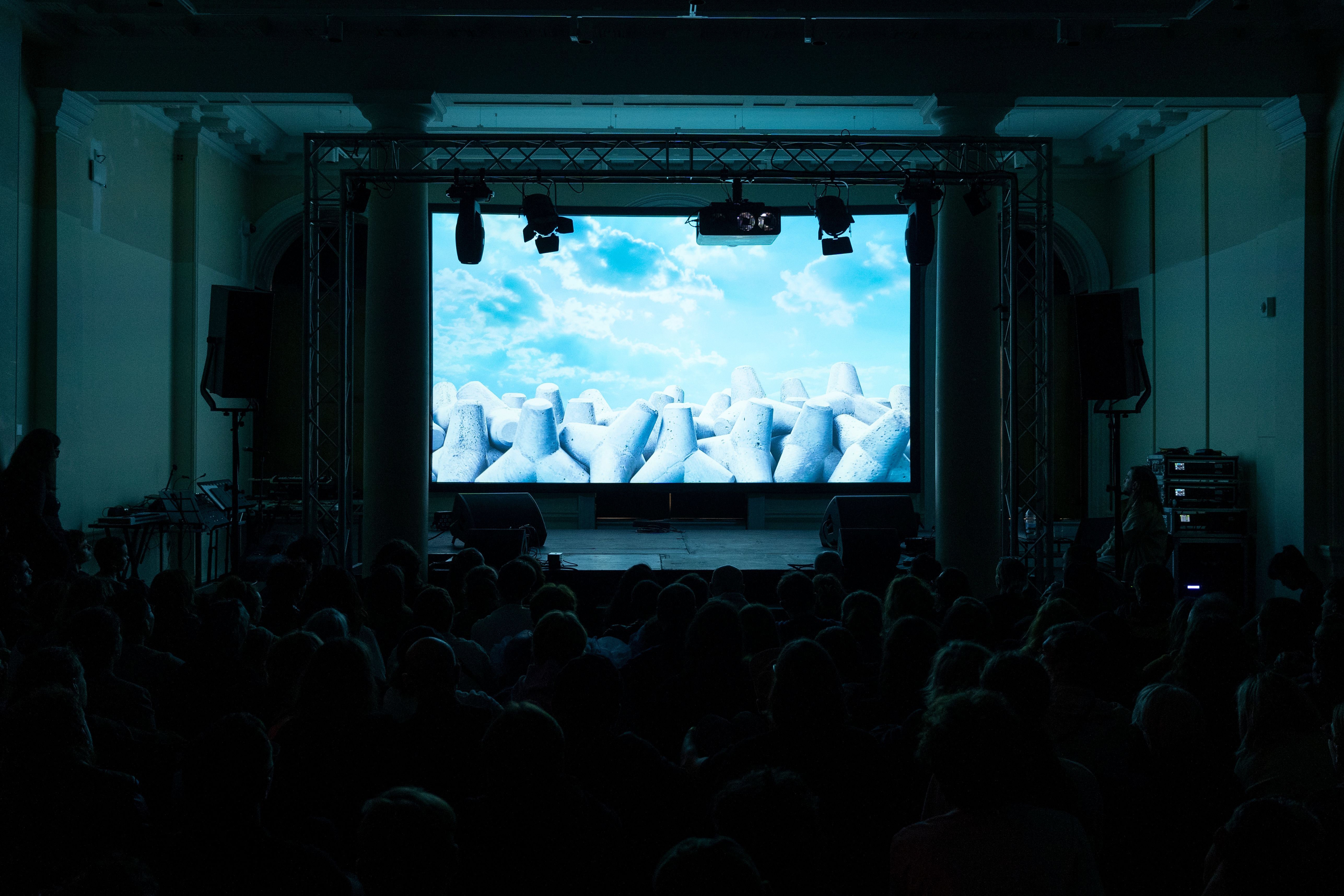 Film screening to a seated audience under a truss-hung projection screen, Assembly 2024, Somerset House Studios