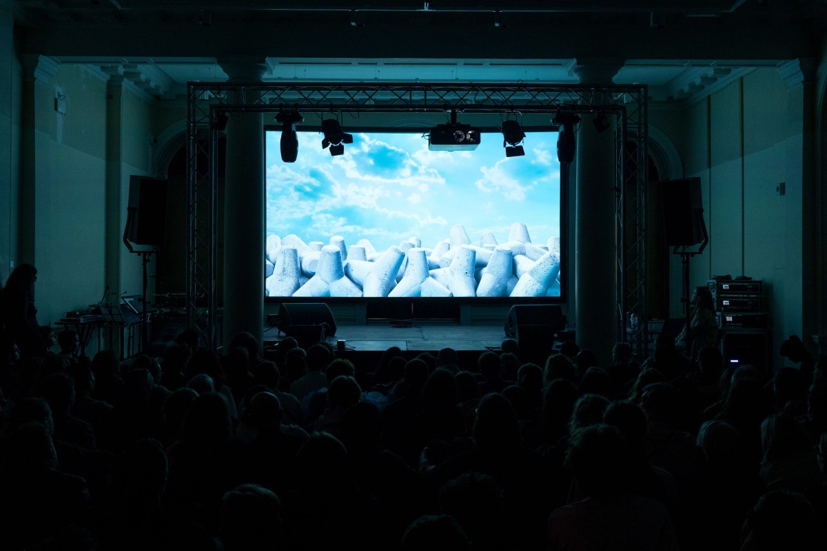 Film screening to a seated audience under a truss-hung projection screen, Assembly 2024, Somerset House Studios