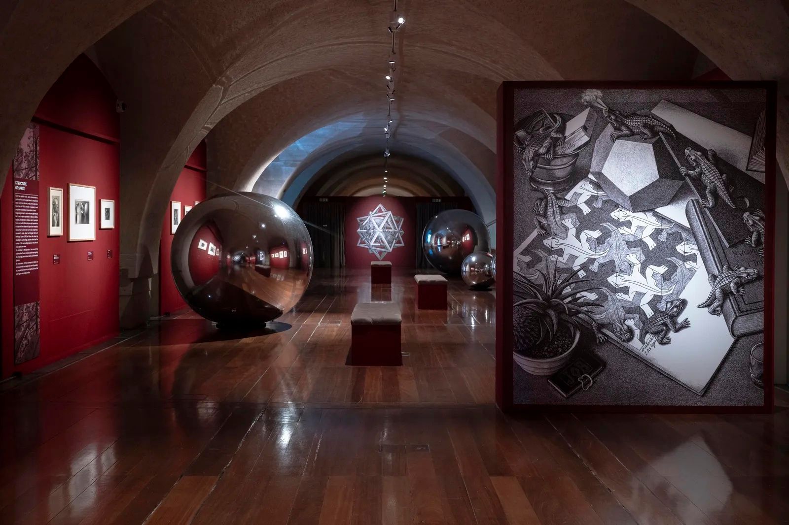 Installation view of M.C. Escher: The Exhibition at Somerset House, with mirrored spheres and an enlarged Escher lithograph.