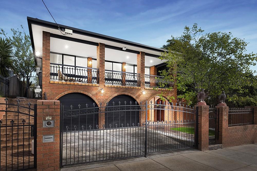 Retained 1970s double-storey brown-brick facade with arched garage and wrought-iron balcony, Brunswick Transformation, Melbourne