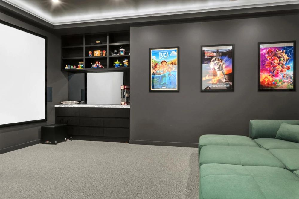 Home theatre with a projector screen, framed posters and a green sofa, Tiffany Walk Residence, Melbourne