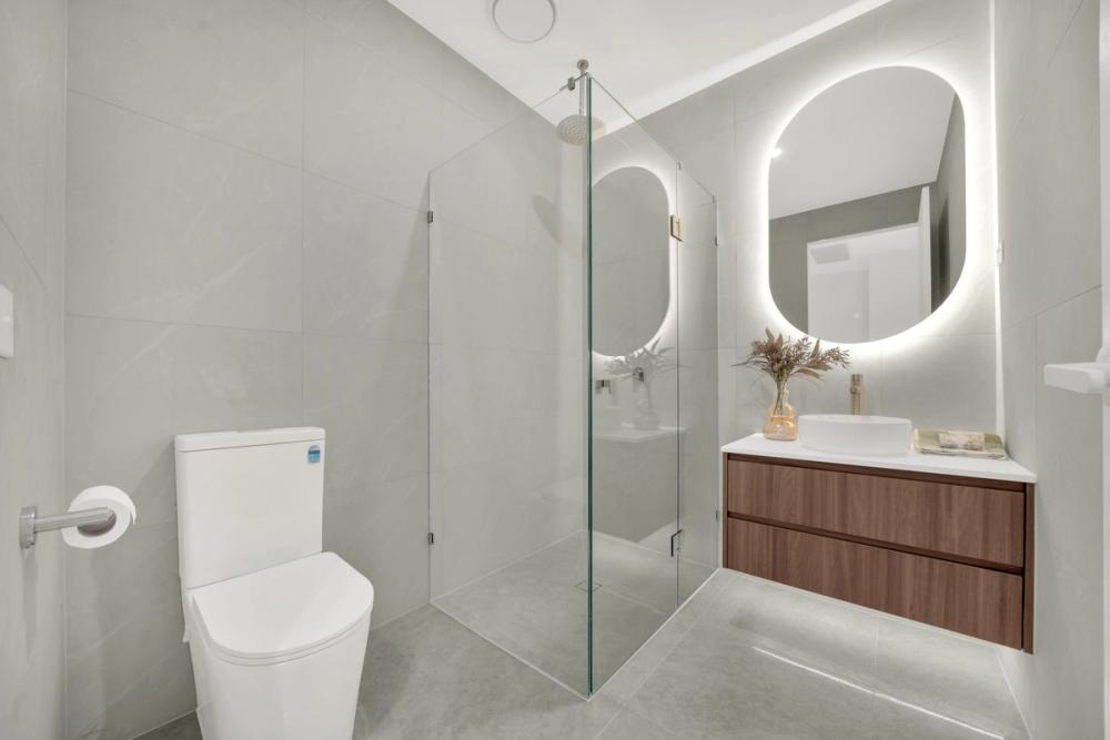 Bathroom with glass shower, backlit oval mirror and timber vanity, Tarneit Cathedral Residence, Melbourne