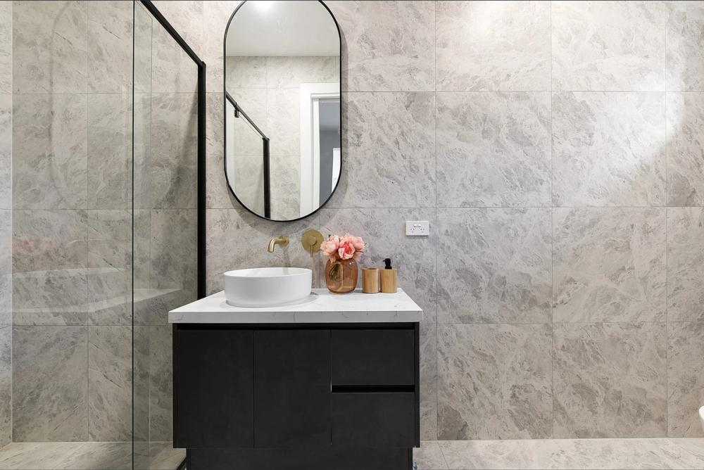 Powder room with marble-look tiles, oval mirror and black vanity with vessel basin, Bentleigh East Development, Melbourne