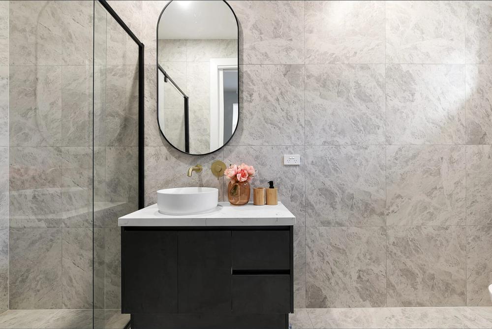 Powder room with marble-look tiles, oval mirror and black vanity with vessel basin, Bentleigh East Development, Melbourne