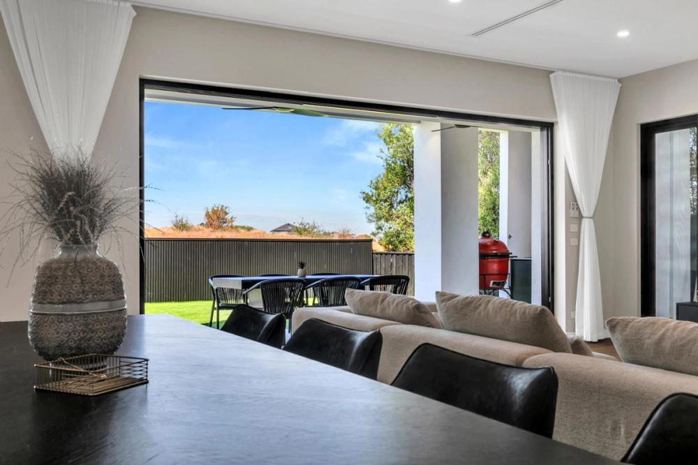 Open living and dining opening to an alfresco lawn through sliding doors, Tiffany Walk Residence, Sanctuary Lakes
